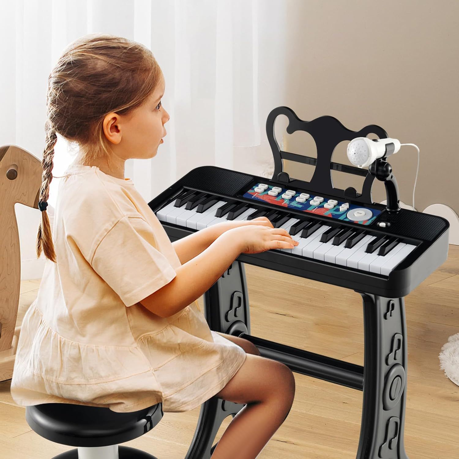 Ein kleines Mädchen sitzt auf einem Hocker und spielt auf einem kleinen schwarzen Spielzeugklavier.