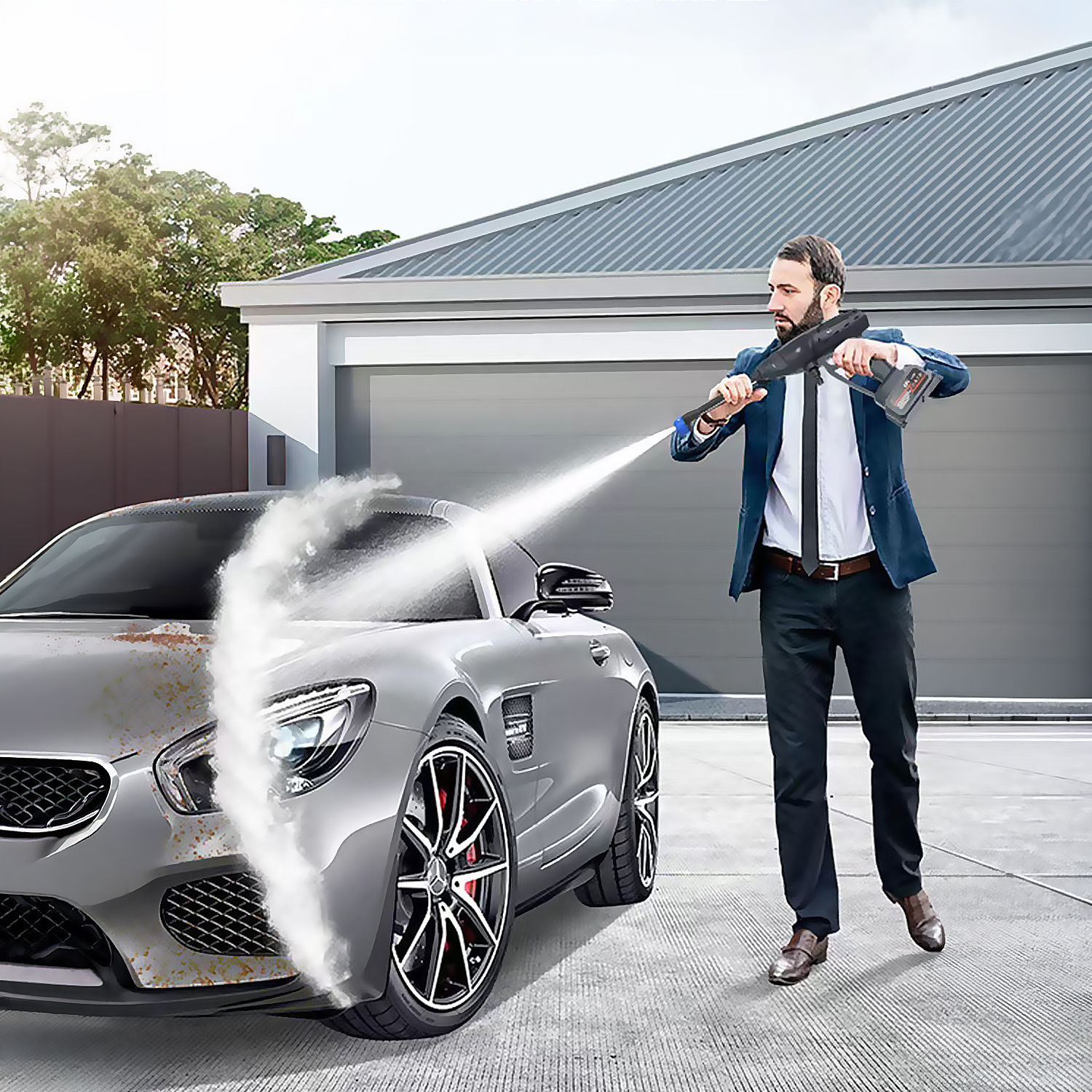 Un hombre con traje usa una hidrolimpiadora para limpiar un coche plateado frente a un garaje.