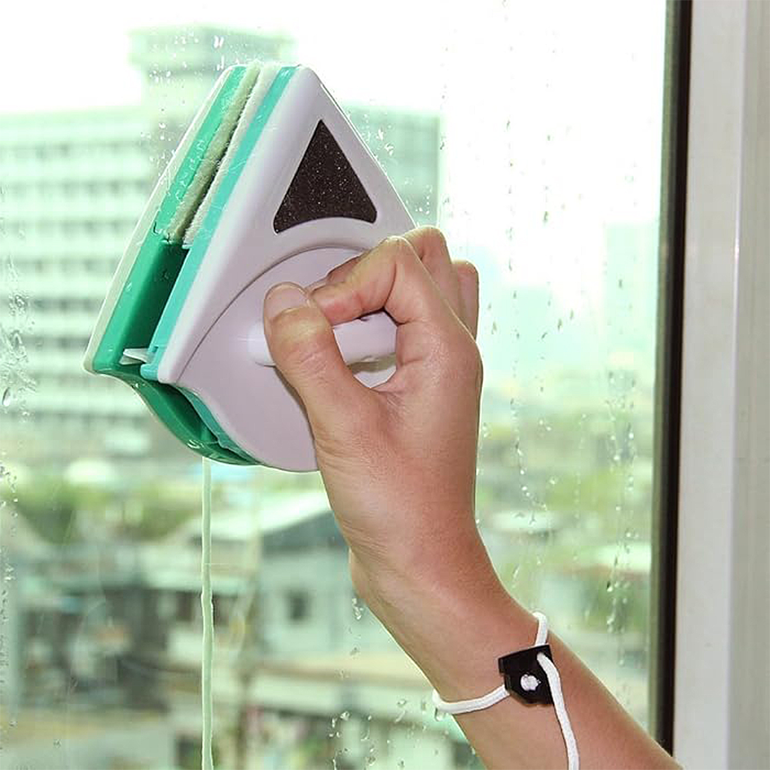 Una mano usa un limpiador de ventanas magnético de doble cara en un vidrio mojado.