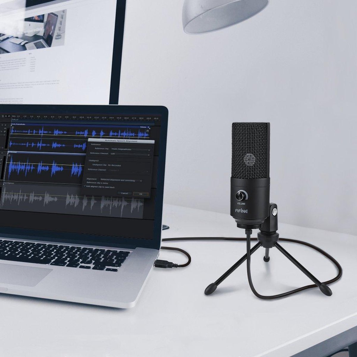 Zwarte Fifine microfoon op een kleinstatief naast een laptop met open audiosoftware.