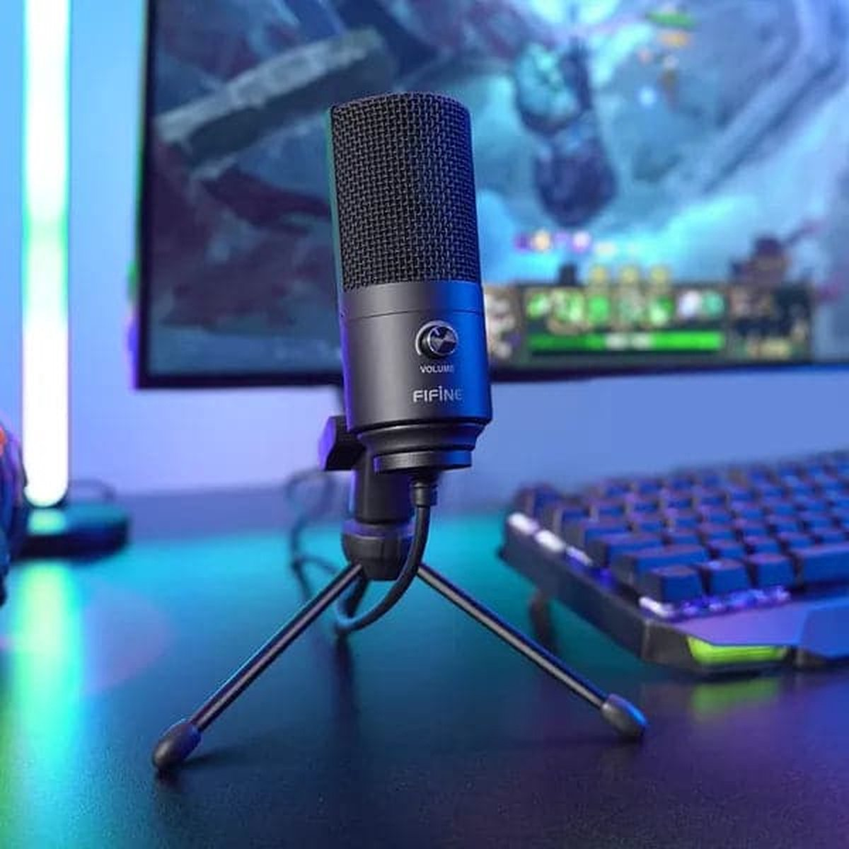 Een zwarte Fifine-microfoon op een klein statief voor een gamemonitor en toetsenbord.