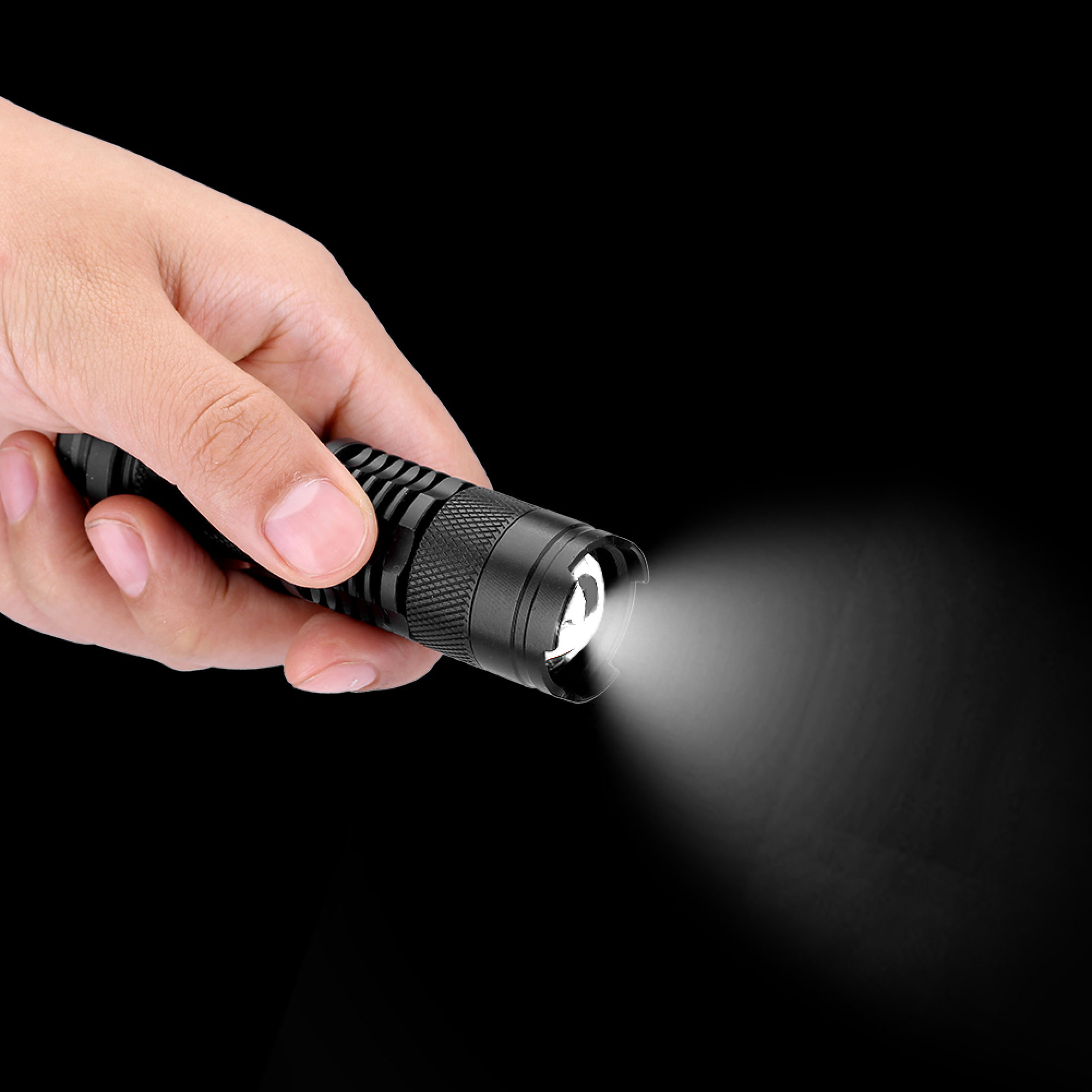 Eine Hand hält eine schwarze Taschenlampe, die einen hellen Lichtstrahl gegen einen dunklen Hintergrund wirft.