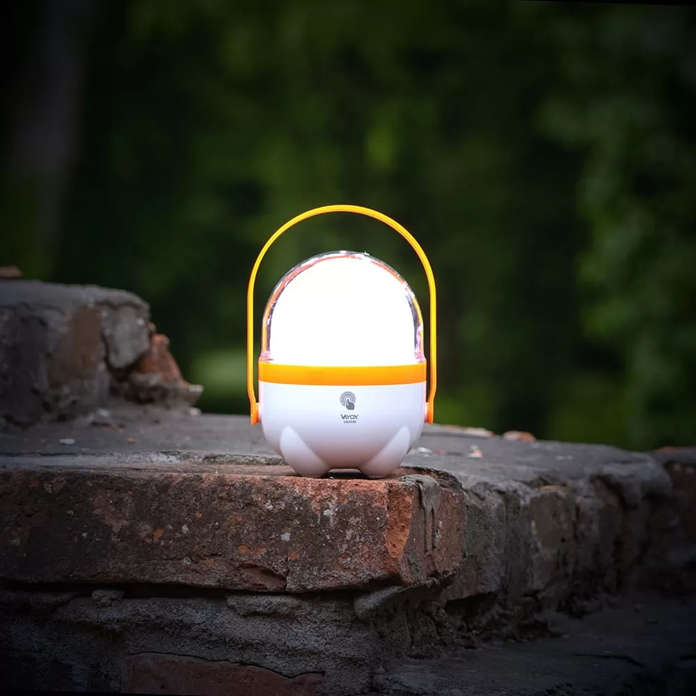 Biało-pomarańczowa lampa przenośna stoi na starym ceglanym murze na zewnątrz.
