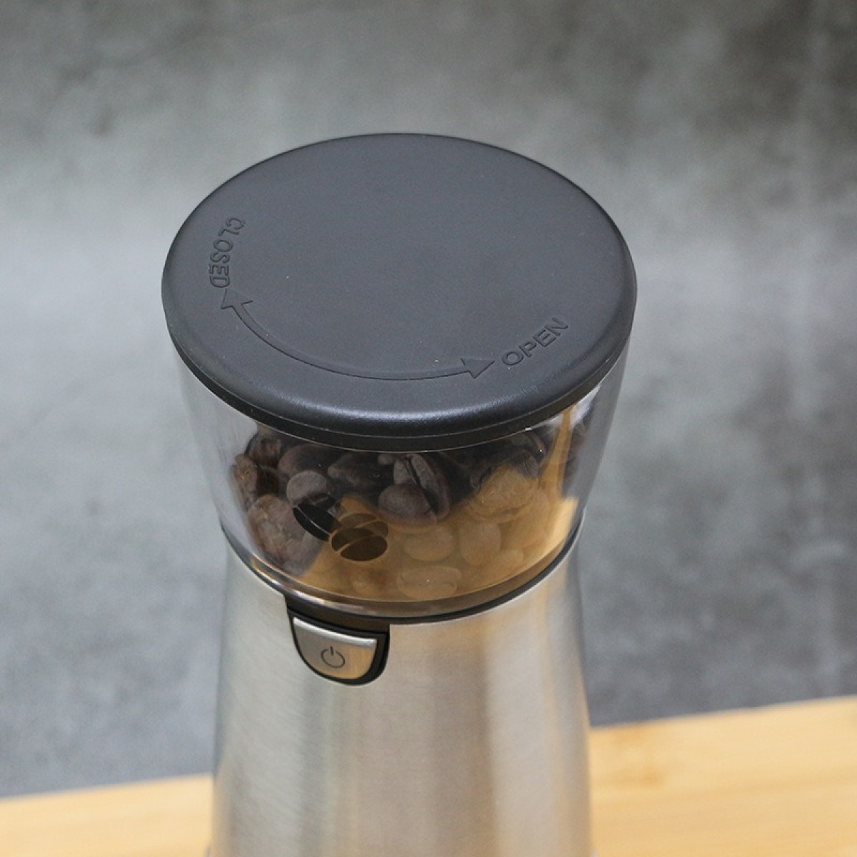 Eine elektrische Kaffeemühle aus Edelstahl mit dunklem Deckel und Bohnen im transparenten Behälter.