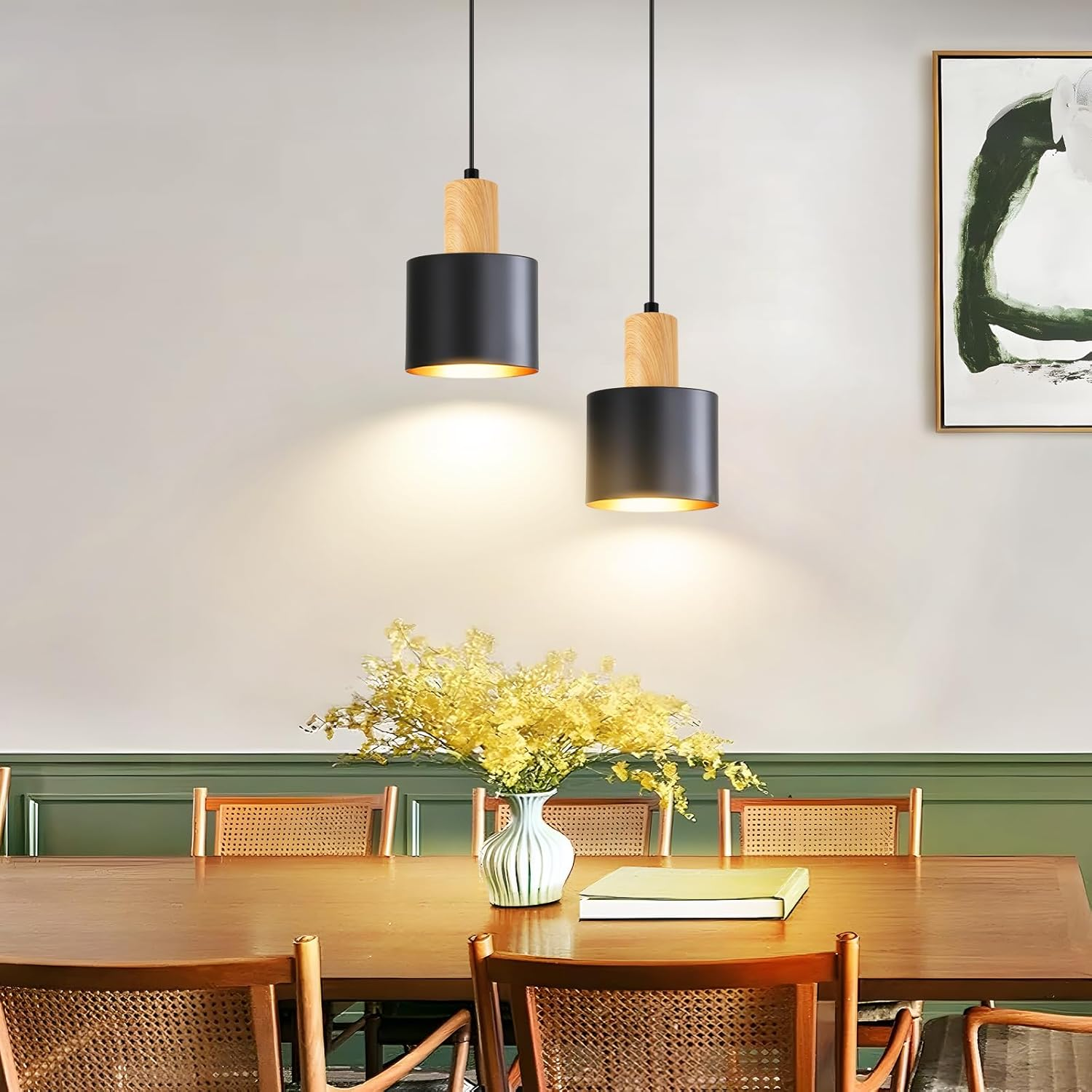 Zwei moderne schwarze Pendelleuchten hängen über einem Holzesstisch mit gelben Blumen und Stühlen.