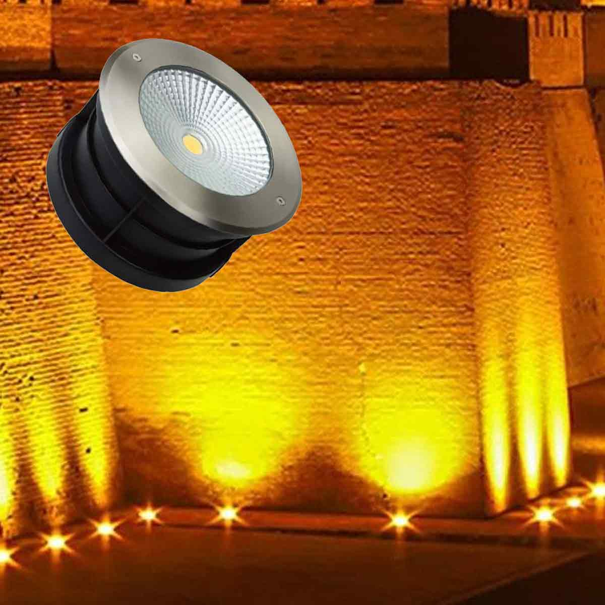 Runde LED-Bodenleuchte vor einer warm erleuchteten Steinwand.