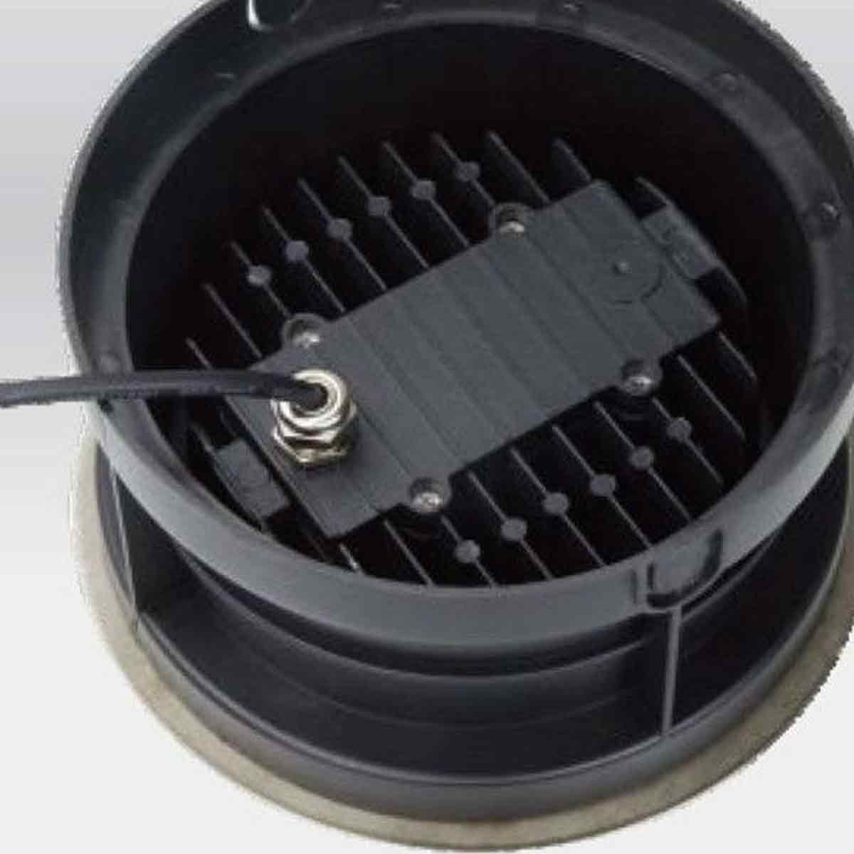 Nahaufnahme eines schwarzen, runden Geräts mit Kühlrippen, einer zentralen Box und einem Netzkabel.