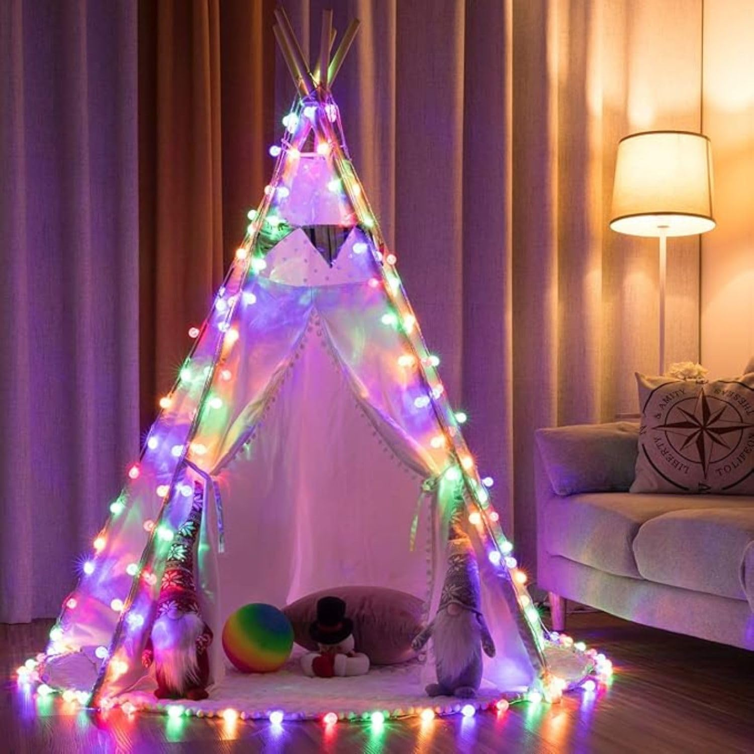 Ein Kindertipi-Zelt mit bunter Lichterkette steht in einem Raum mit Sofa und Lampe.