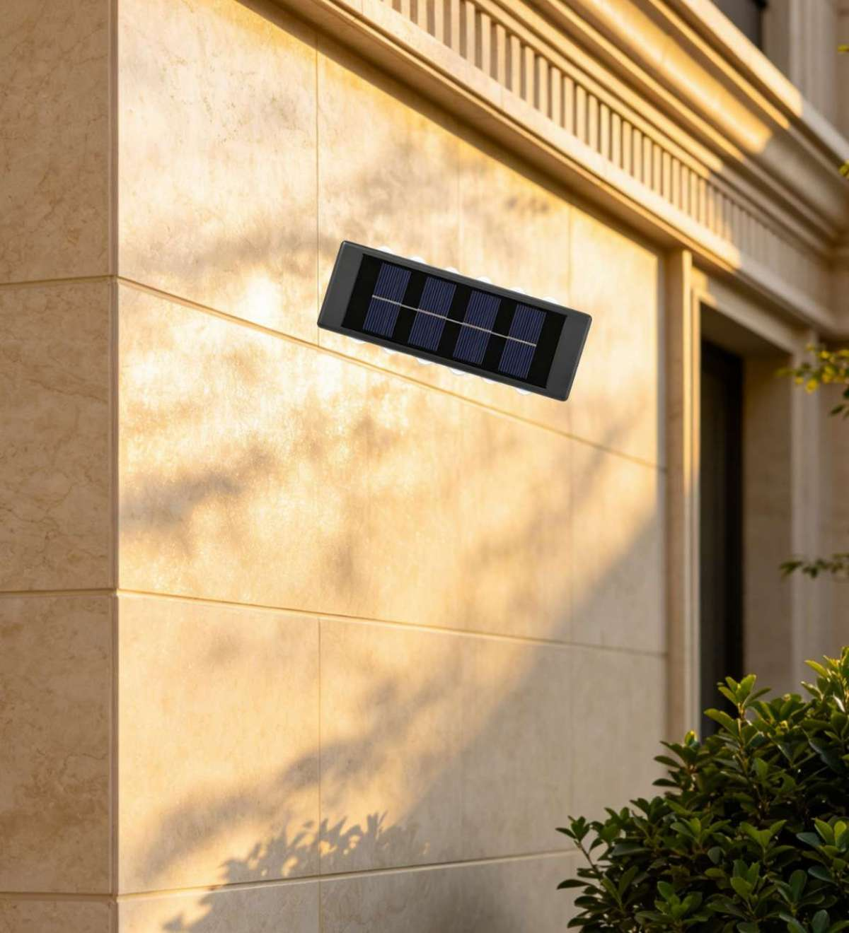 Eine schwarze Solar-Wandleuchte ist an einer hellen, beige gefliesten Außenwand montiert, im Hintergrund ist Grün zu sehen.