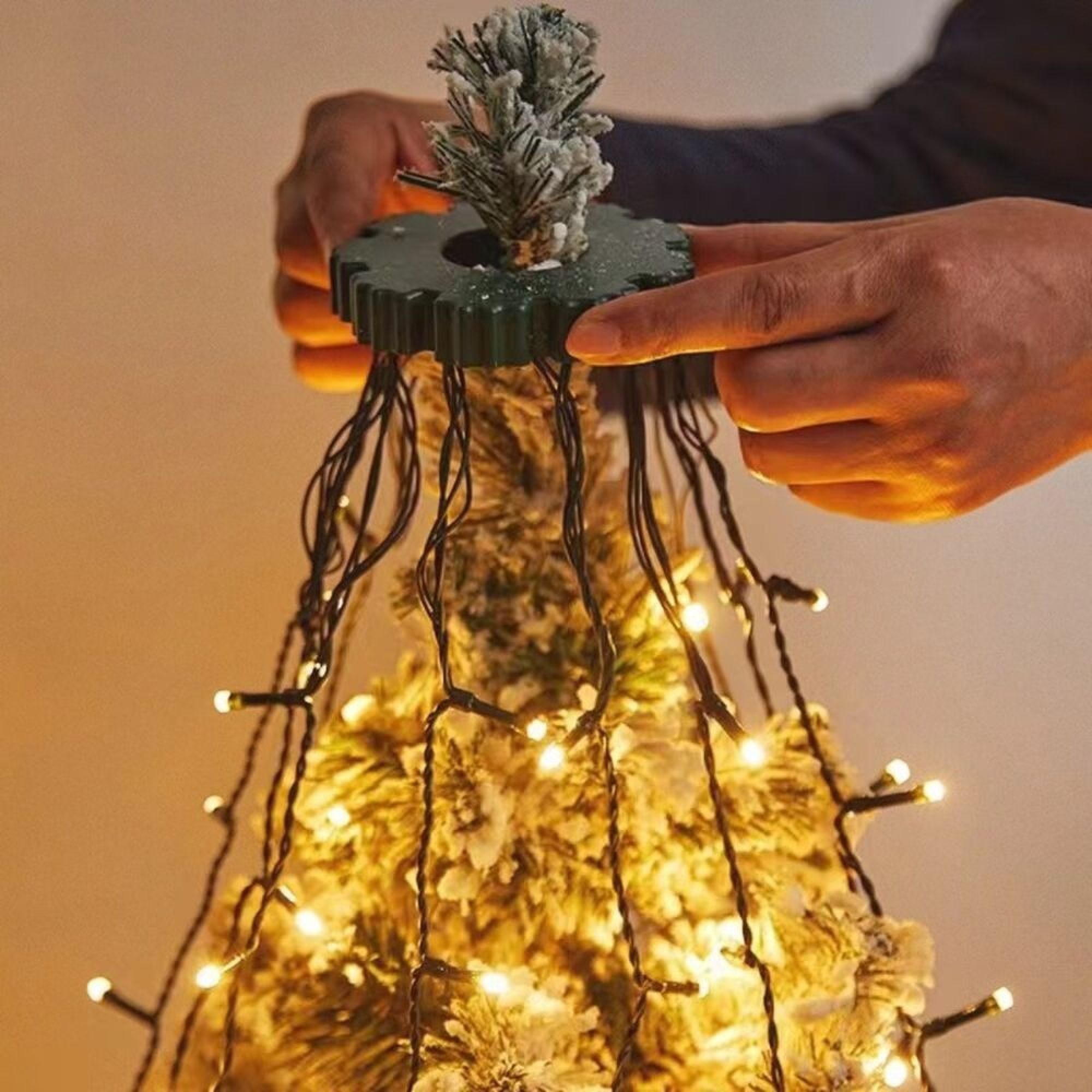 Hände platzieren einen grünen Ring mit hängenden Lichterketten auf der Spitze eines Weihnachtsbaums.