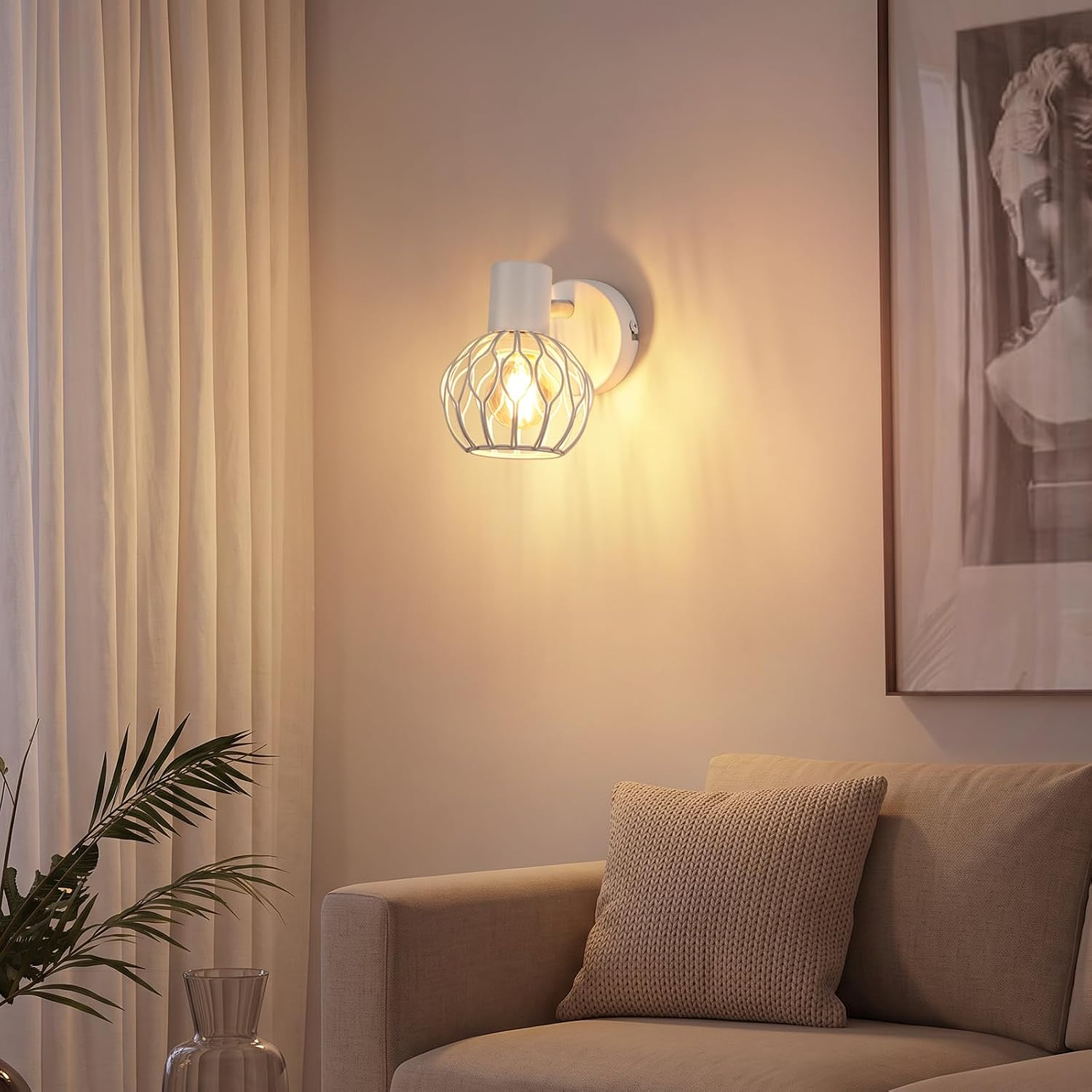 Eine weiße Wandleuchte mit kugelförmigem Gitter schimmert warm an einer beigen Wand über einem Sofa.