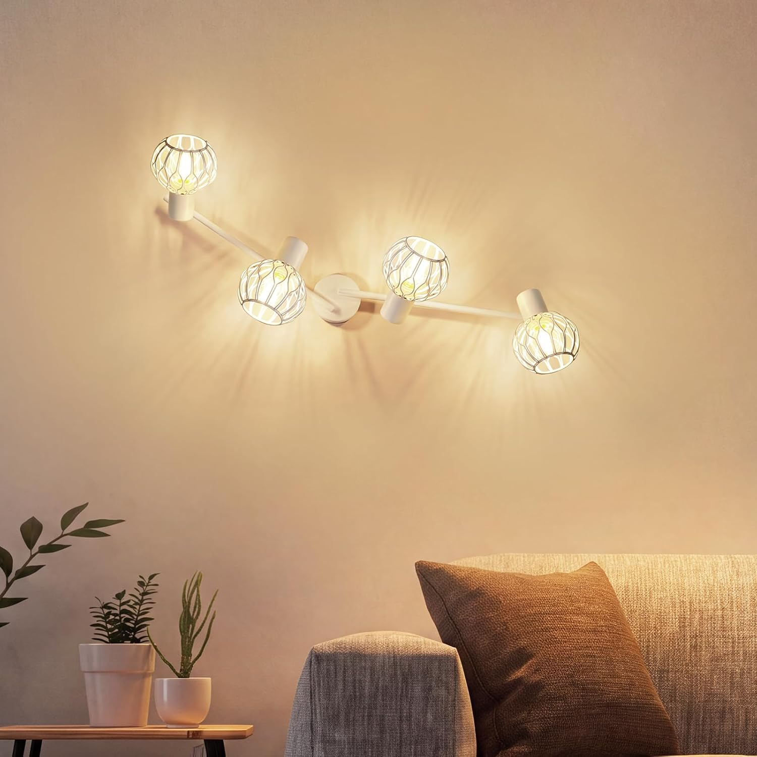 Eine weiße Vier-Flammen-Wandleuchte an einer beige Wand wirft ein warmes Licht über ein graues Sofa.