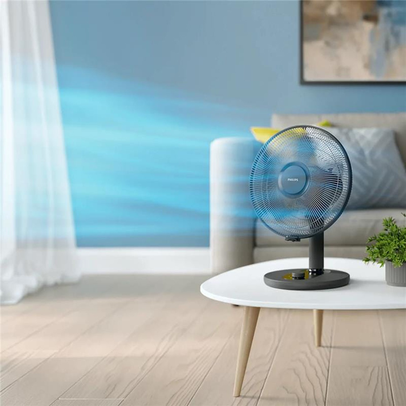 Ein blauer Philips Tischventilator auf einem weißen Tisch, der einen kühlen Luftstrom erzeugt.