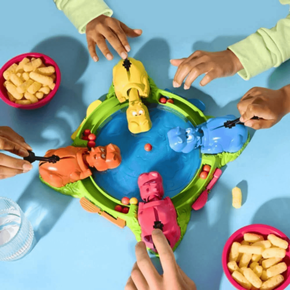 Vier Personen spielen ein farbenfrohes Nilpferd-Spiel auf einem blauen Tisch mit Snacks.
