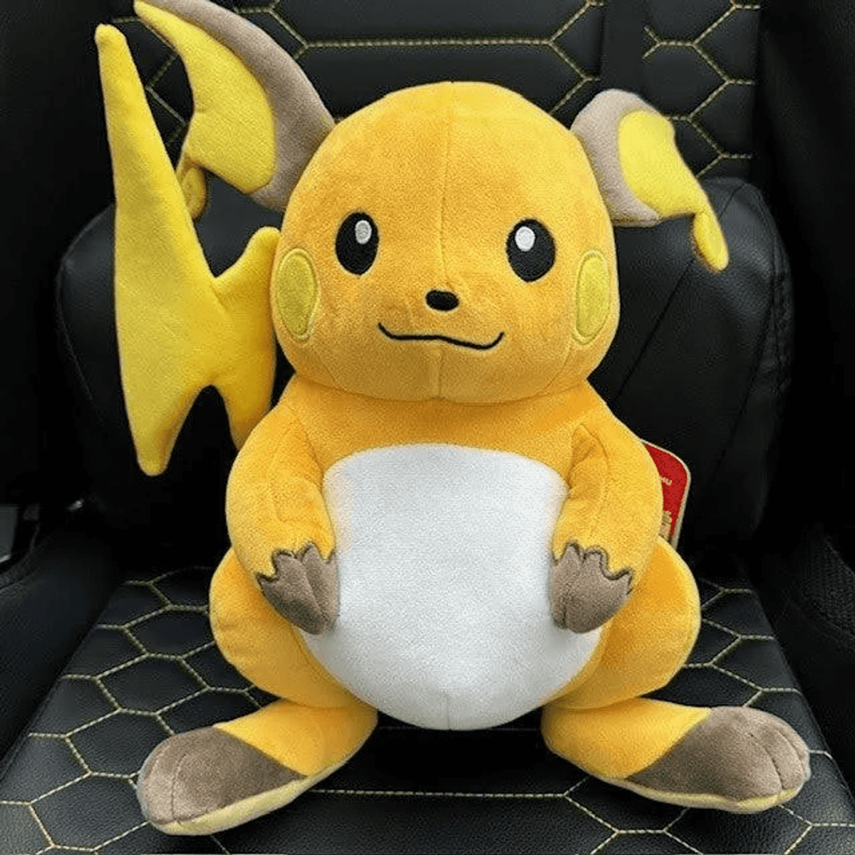 Ein gelbes, plüschiges Raichu-Stofftier sitzt auf einem schwarzen Sitz mit gelben Nähten.