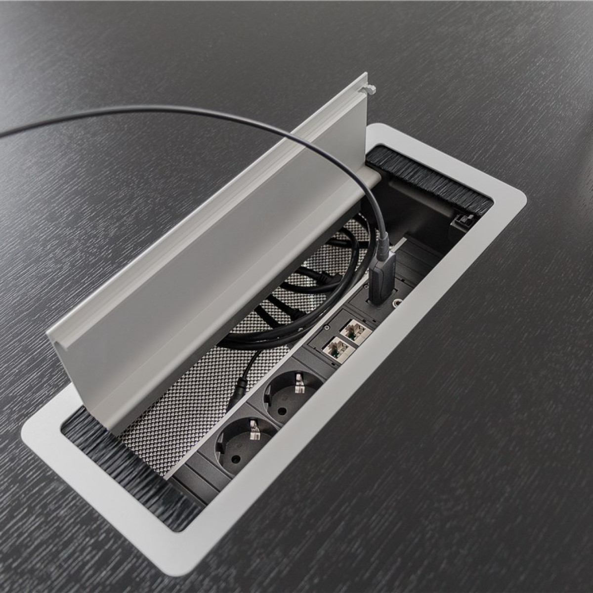 Eine offene Kabeldurchführung in einem schwarzen Holztisch mit Steckdosen und Ethernet-Anschlüssen.