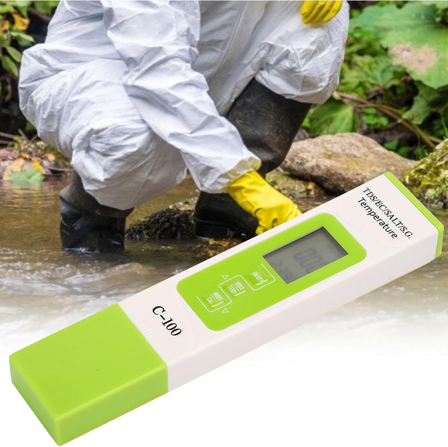 Ein C-100 Wassertester im Vordergrund, während eine Person im Schutzanzug im Hintergrund an einem Bach kniet.