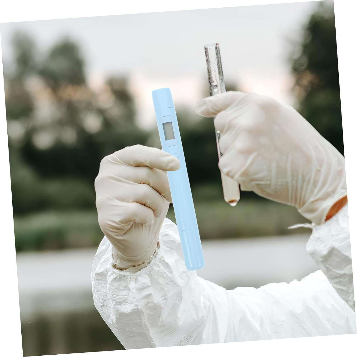 Eine Person im Schutzanzug hält ein digitales Testgerät und ein Reagenzglas mit Wasser.
