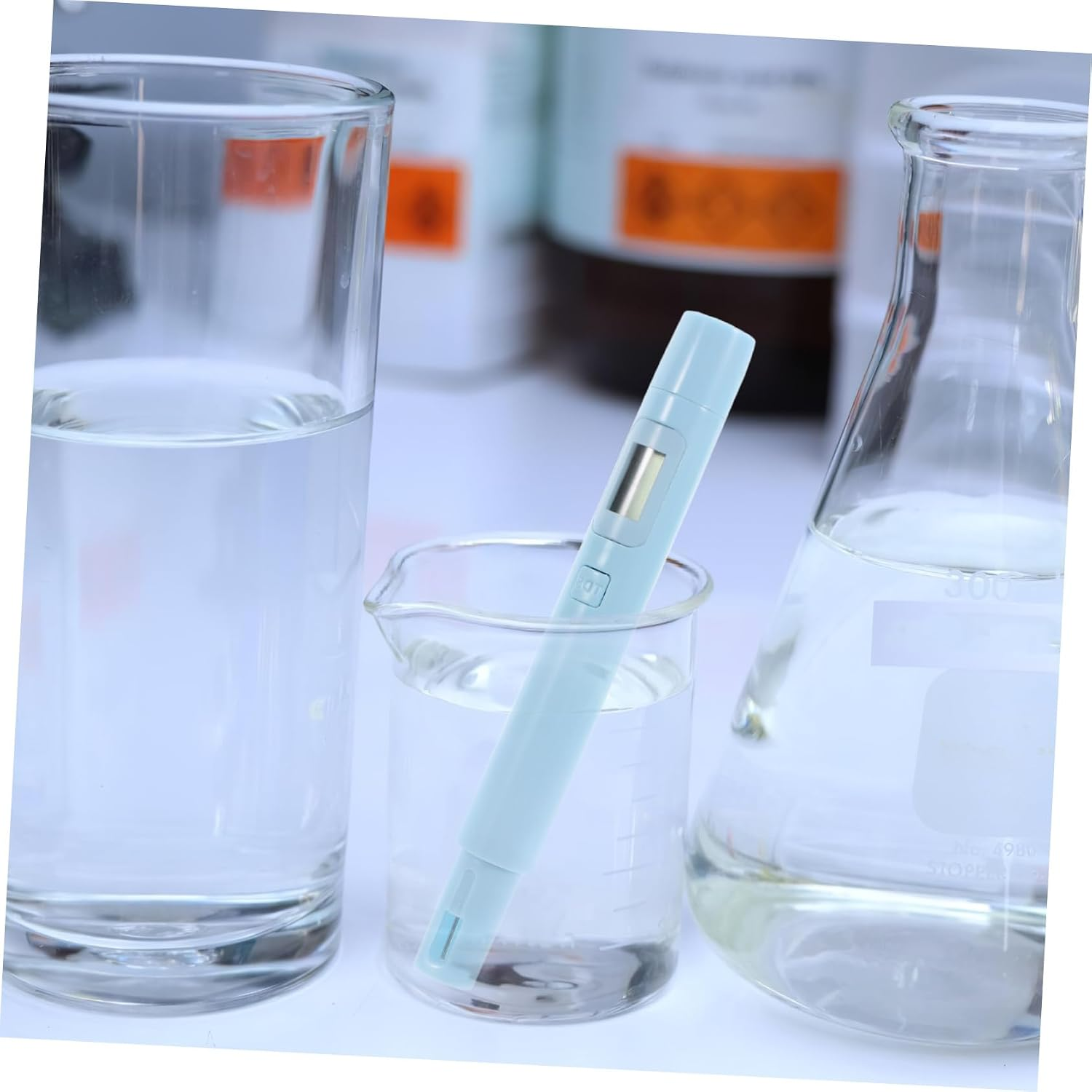Ein hellblauer digitaler Tester steht in einem Becherglas mit Wasser, flankert von einem Glas und einem Kolben.