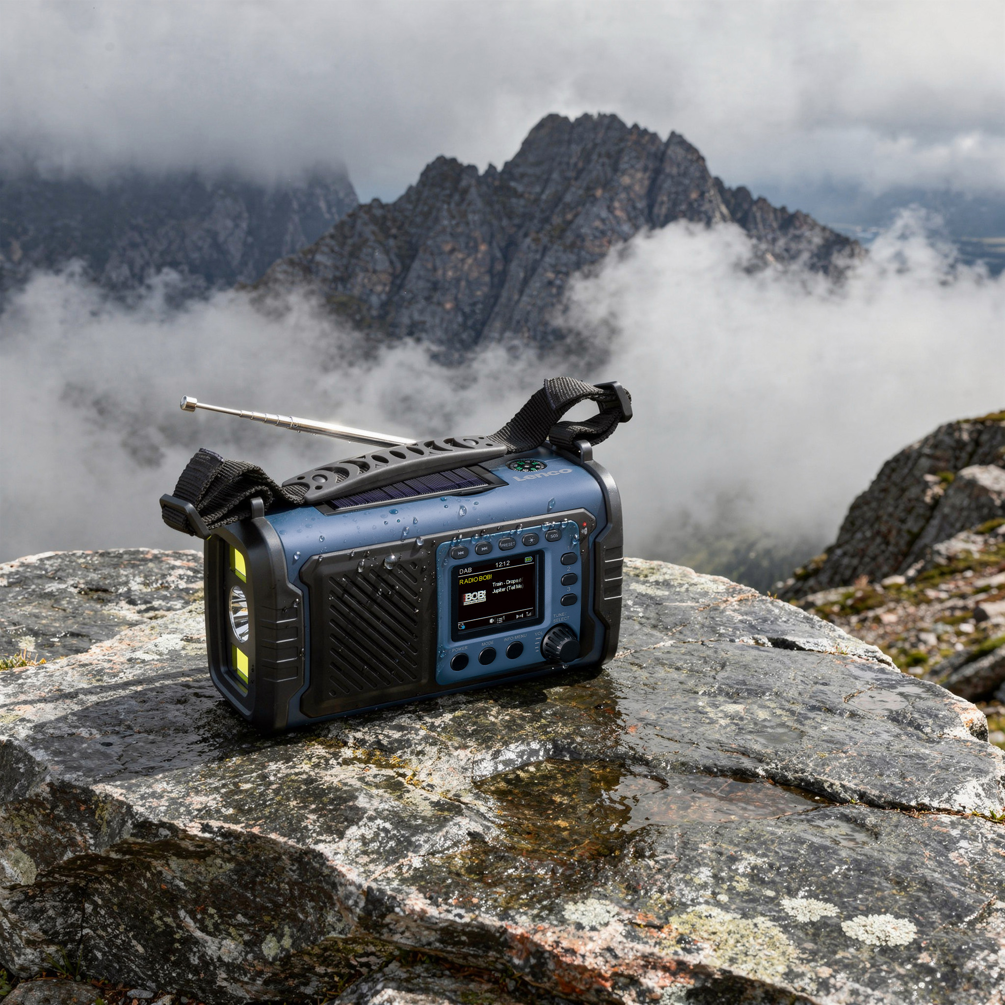 Ein blaues Notrufradio mit Antenne auf nassem Fels, im Hintergrund neblige, felsige Berge.