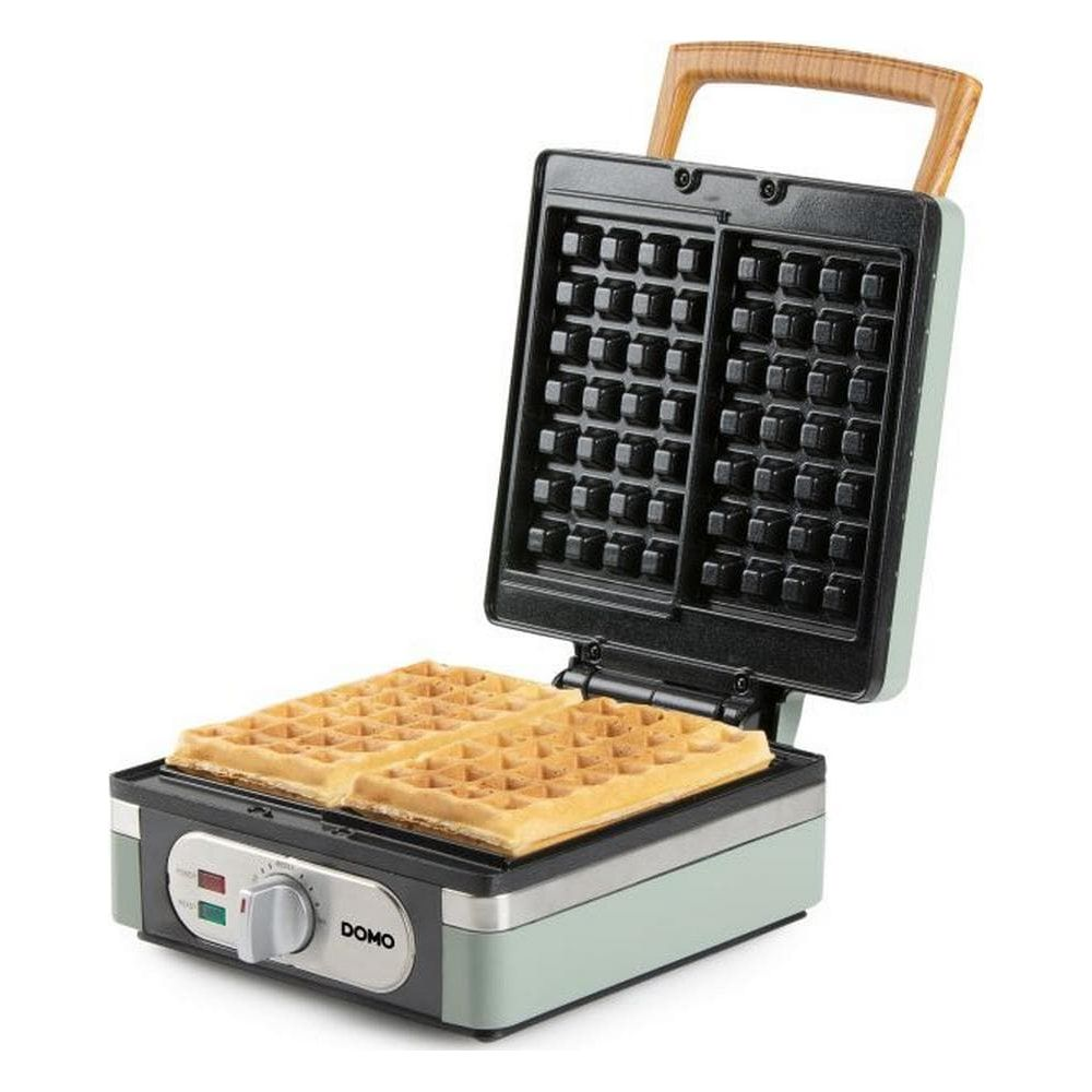 Una piastra per waffle verde menta aperta con due waffle appena sfornati su sfondo bianco.