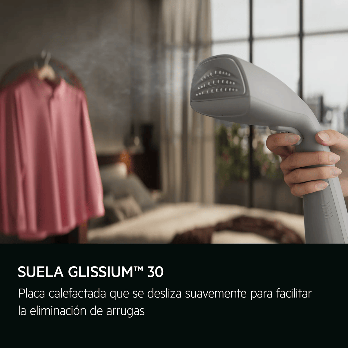 Cepillo de vapor de mano alisando una camisa rosa en un dormitorio.