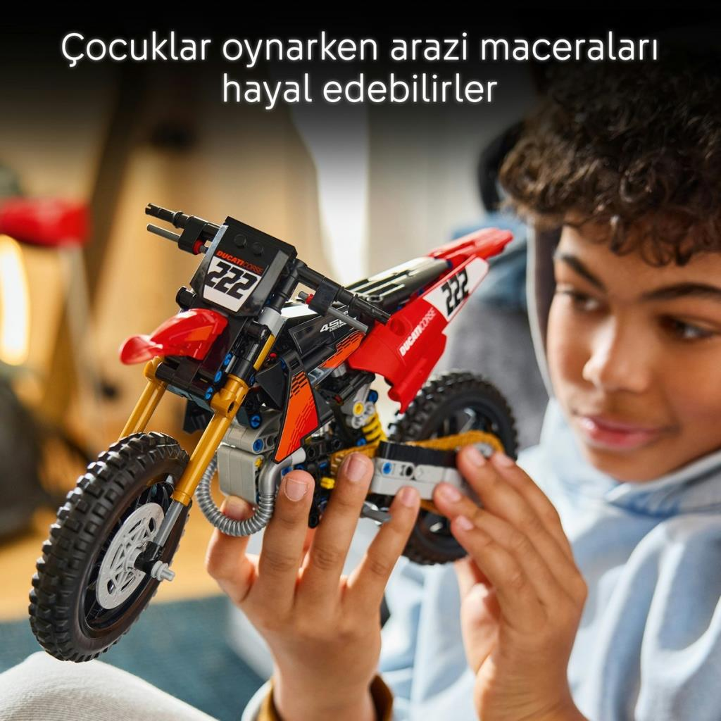 Bir çocuk kırmızı bir LEGO motosiklet inşa ediyor ve gülümsüyor.