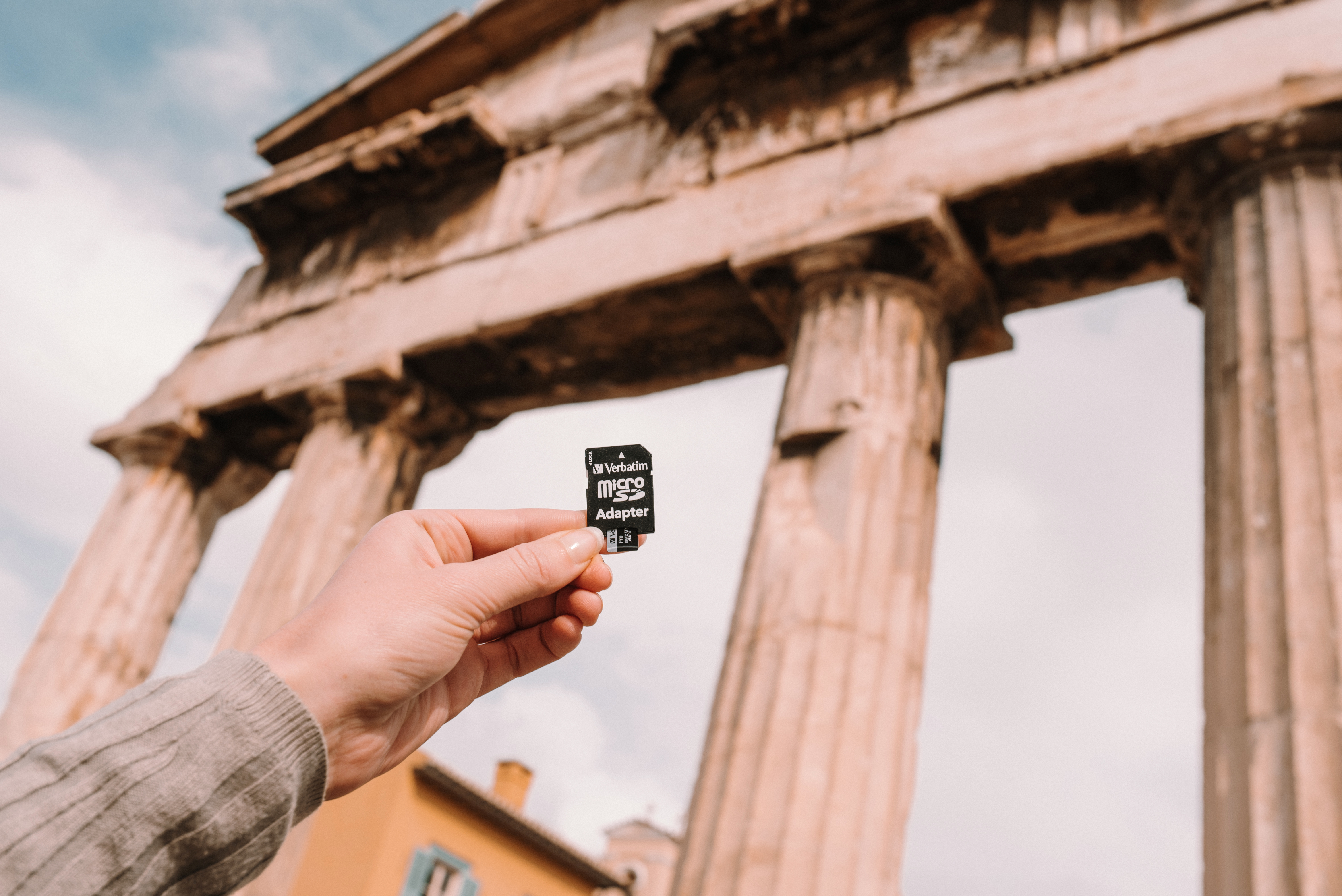 Mano che tiene un adattatore micro SD Verbatim davanti a antiche colonne.