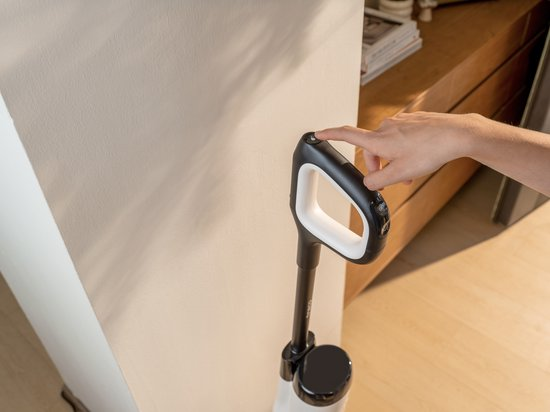 Une main appuie sur le bouton d'alimentation d'un manche d'aspirateur noir et blanc.