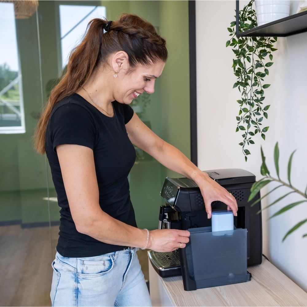 A woman in a black t-shirt and jeans inserts a water tank into a coffee machine.
