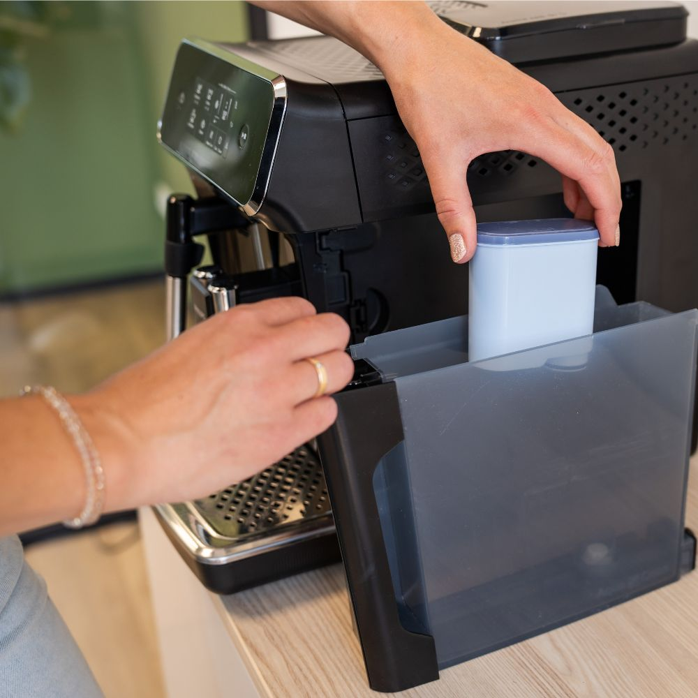 A person inserts a blue water filter into the water tank of a modern coffee machine.