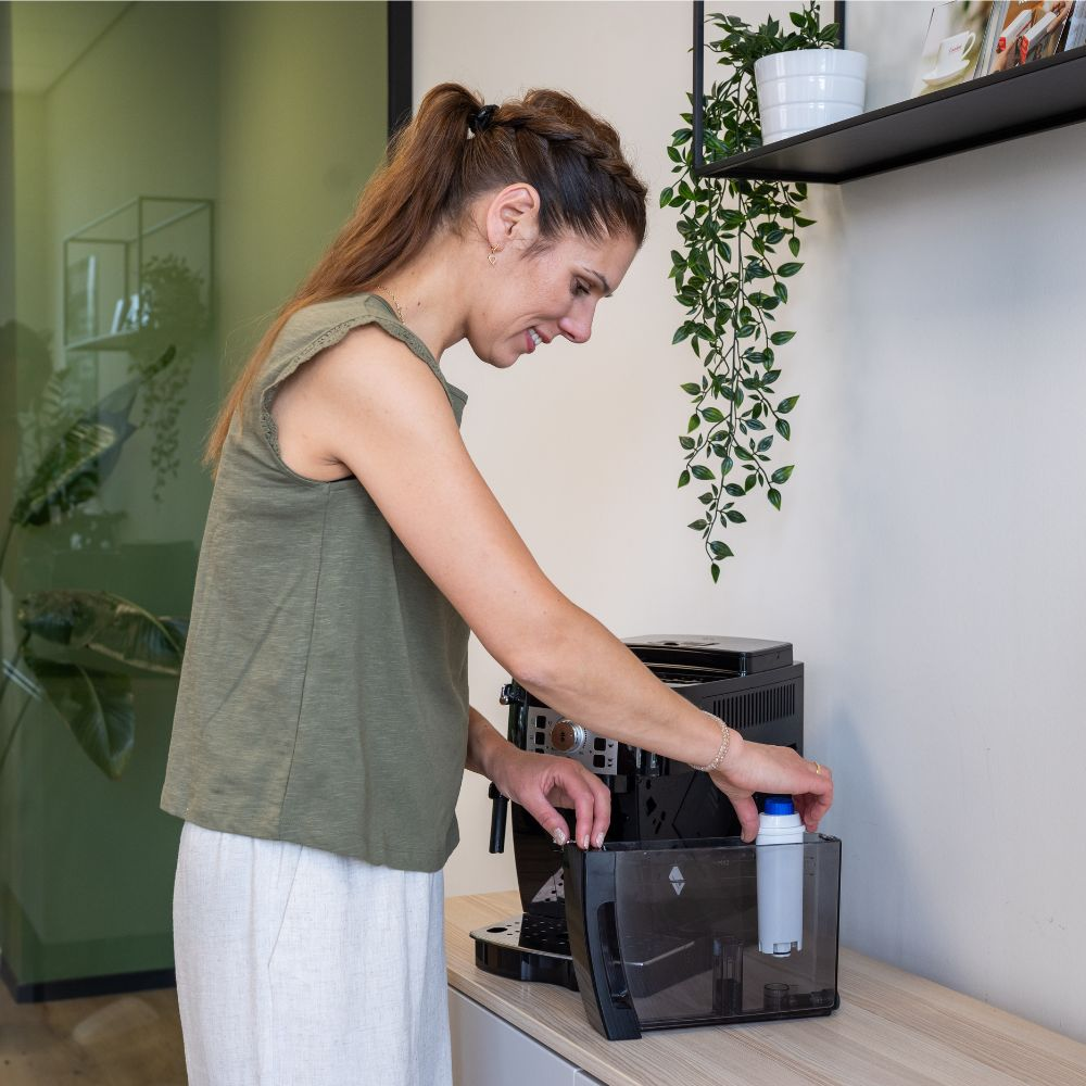 A woman in a green top inserts a filter into a coffee machine's water tank.