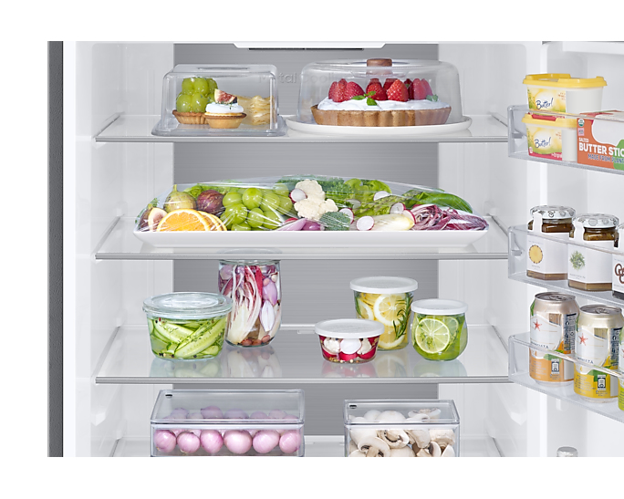 Gut gefüllter Kühlschrank mit frischem Obst, Gemüse, Kuchen, Gläsern und Getränken auf den Glasböden.