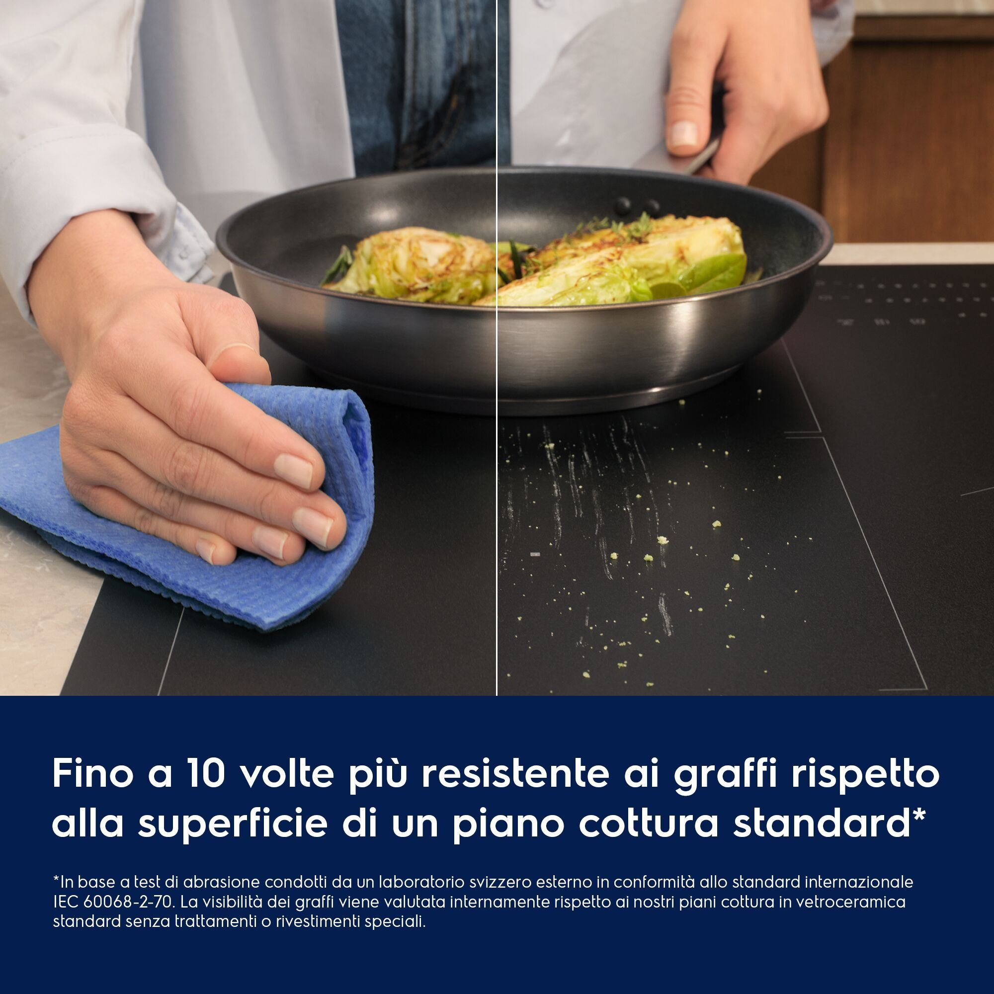 Una persona pulisce un piano cottura nero con un panno blu, sopra una padella con cibo.