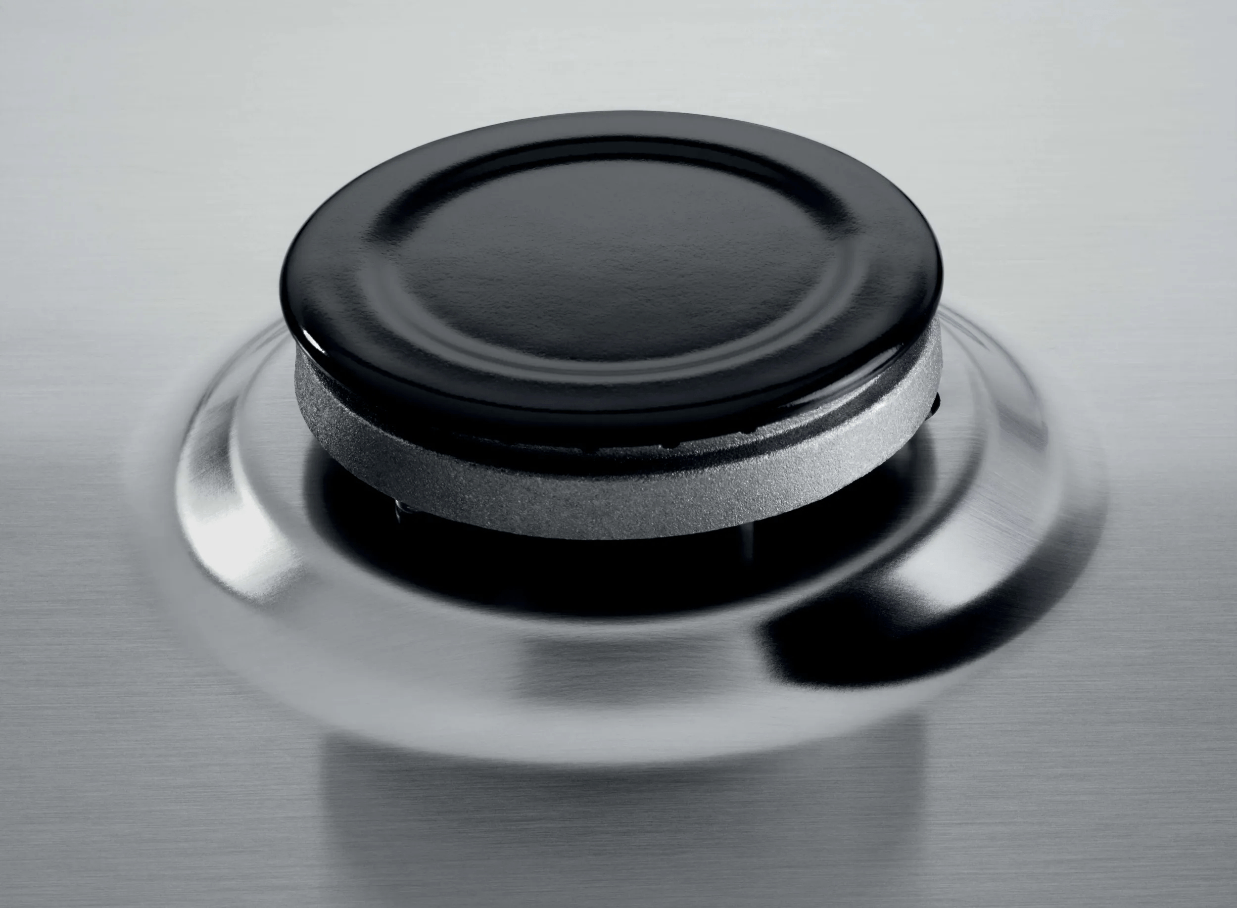 Un quemador de gas negro y plateado brillante sobre una superficie de acero inoxidable cepillado.