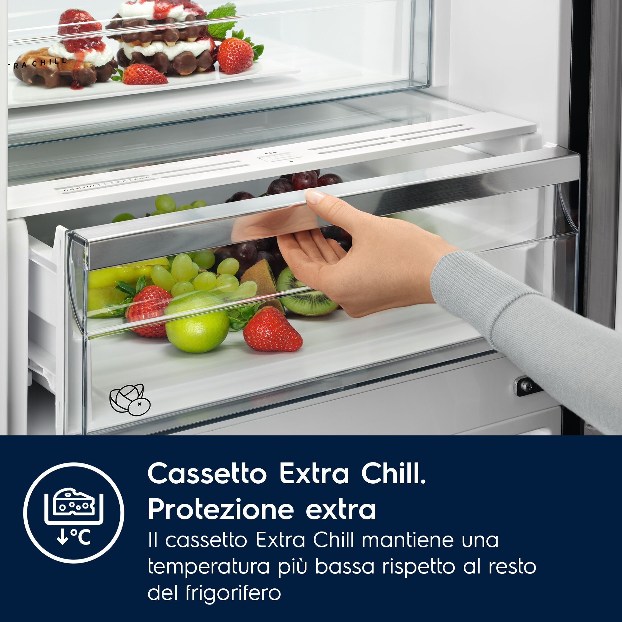 Una mano apre il cassetto verdura del frigorifero pieno di frutta fresca.