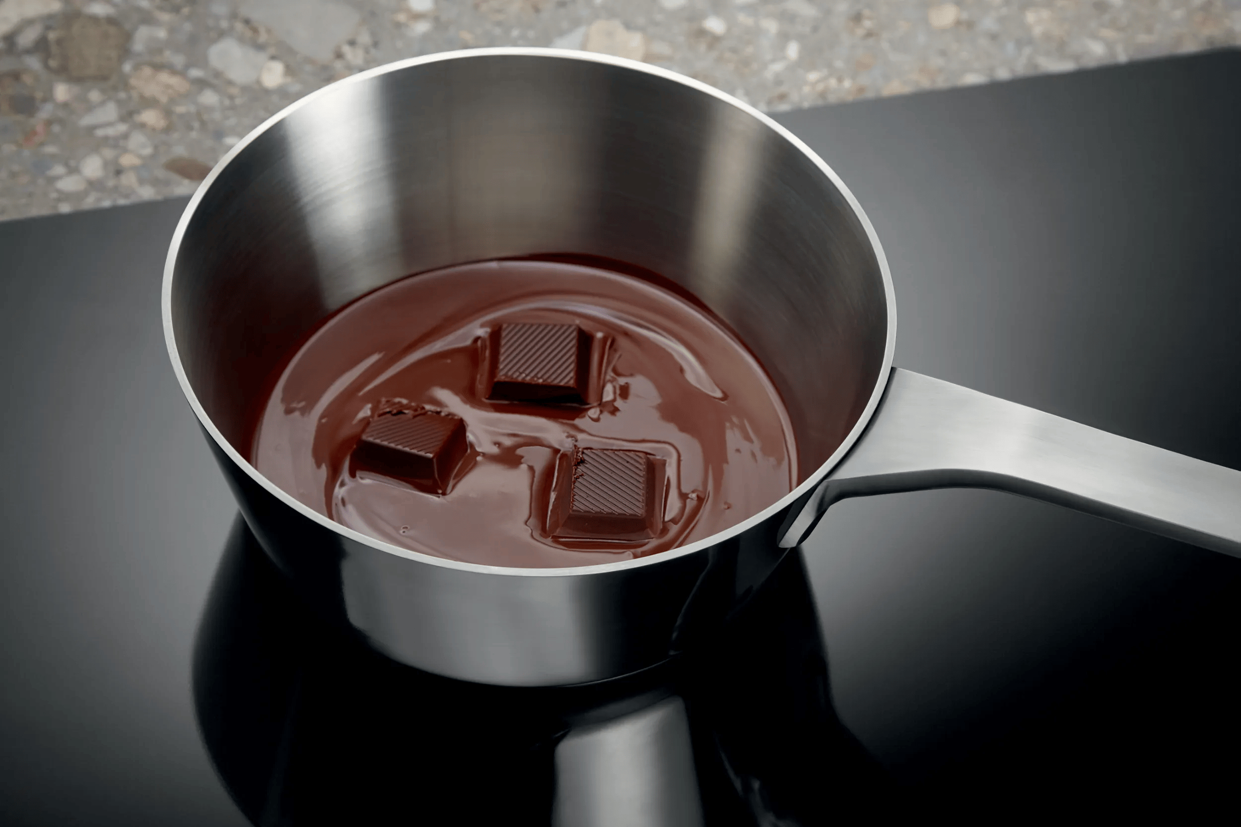 Tre quadratini di cioccolato si sciolgono in una pentola su un piano cottura.