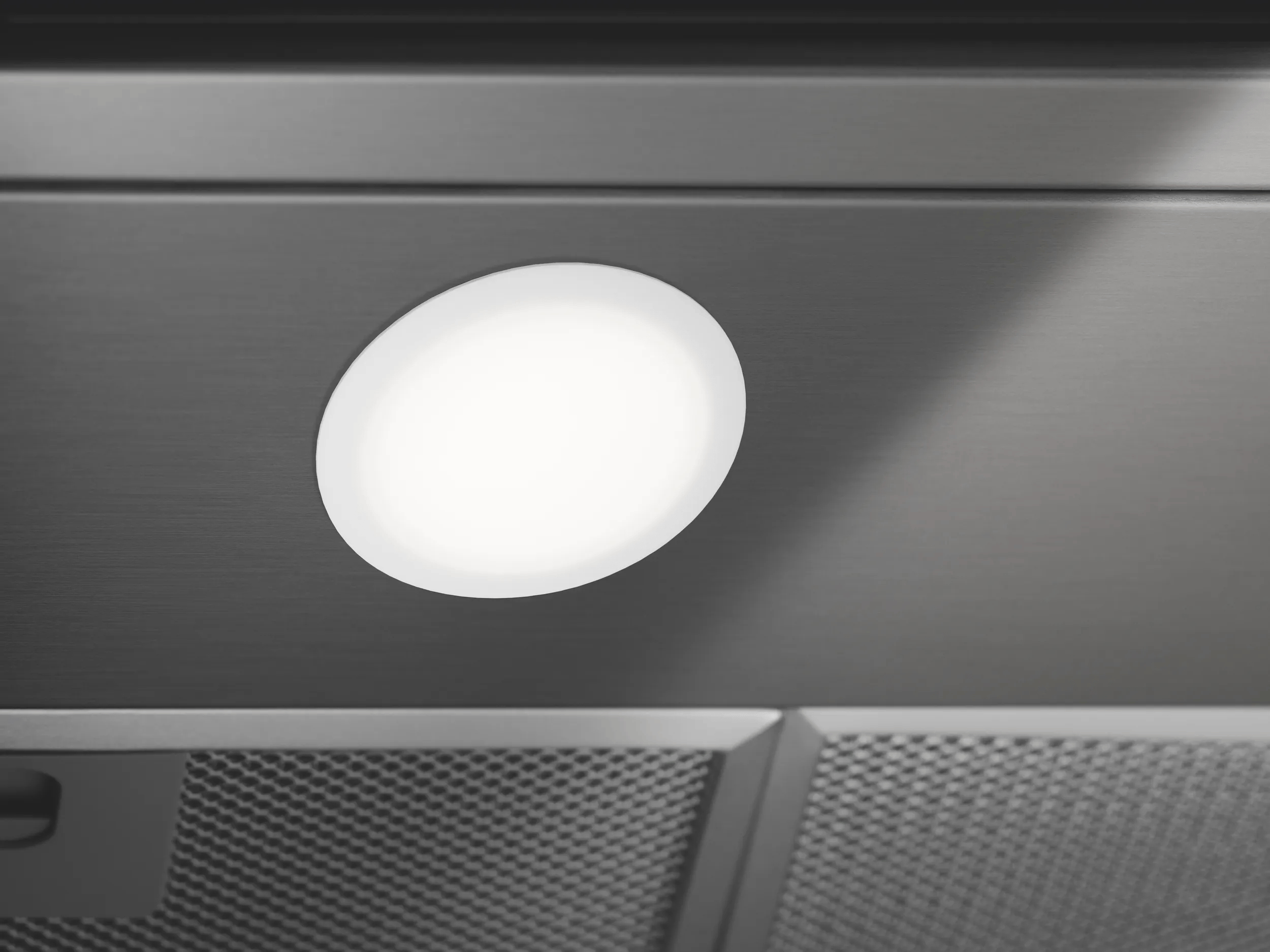 Una luz LED redonda y brillante integrada en una campana extractora de metal gris.