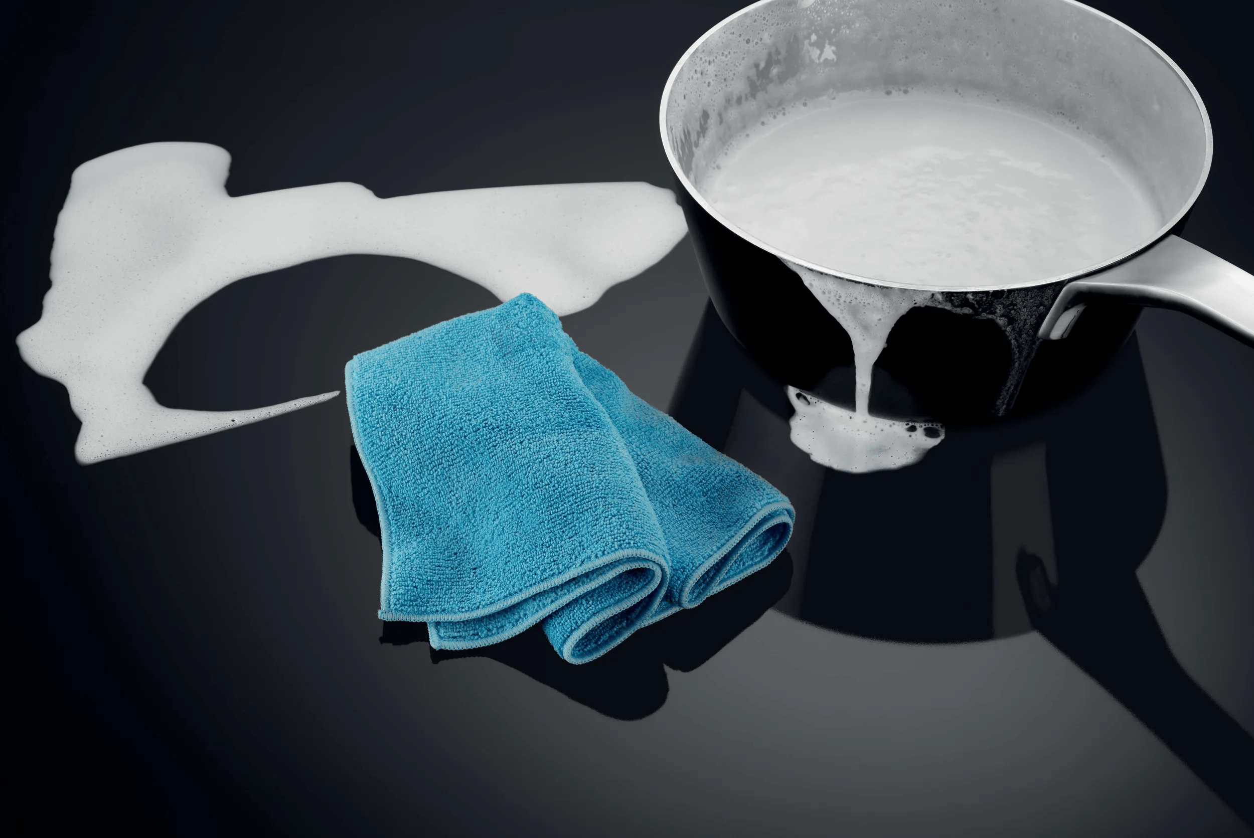 Un panno blu, una pentola piena di liquido bianco e schiuma su un piano cottura nero.