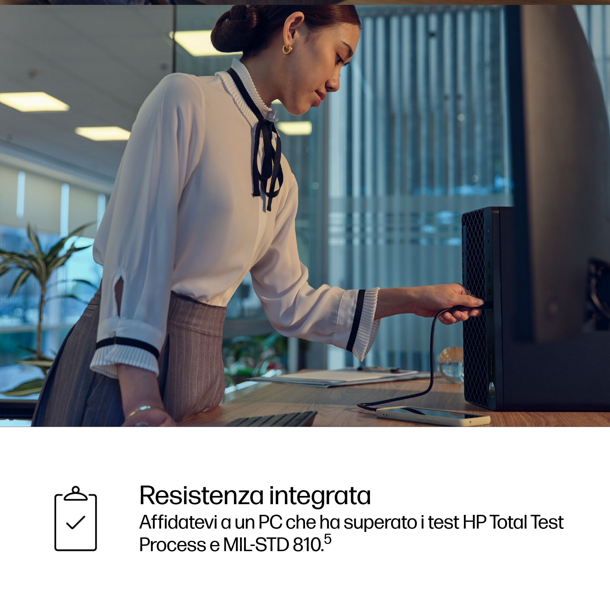 Una donna con camicetta bianca collega un cavo a un PC desktop in un ufficio moderno.