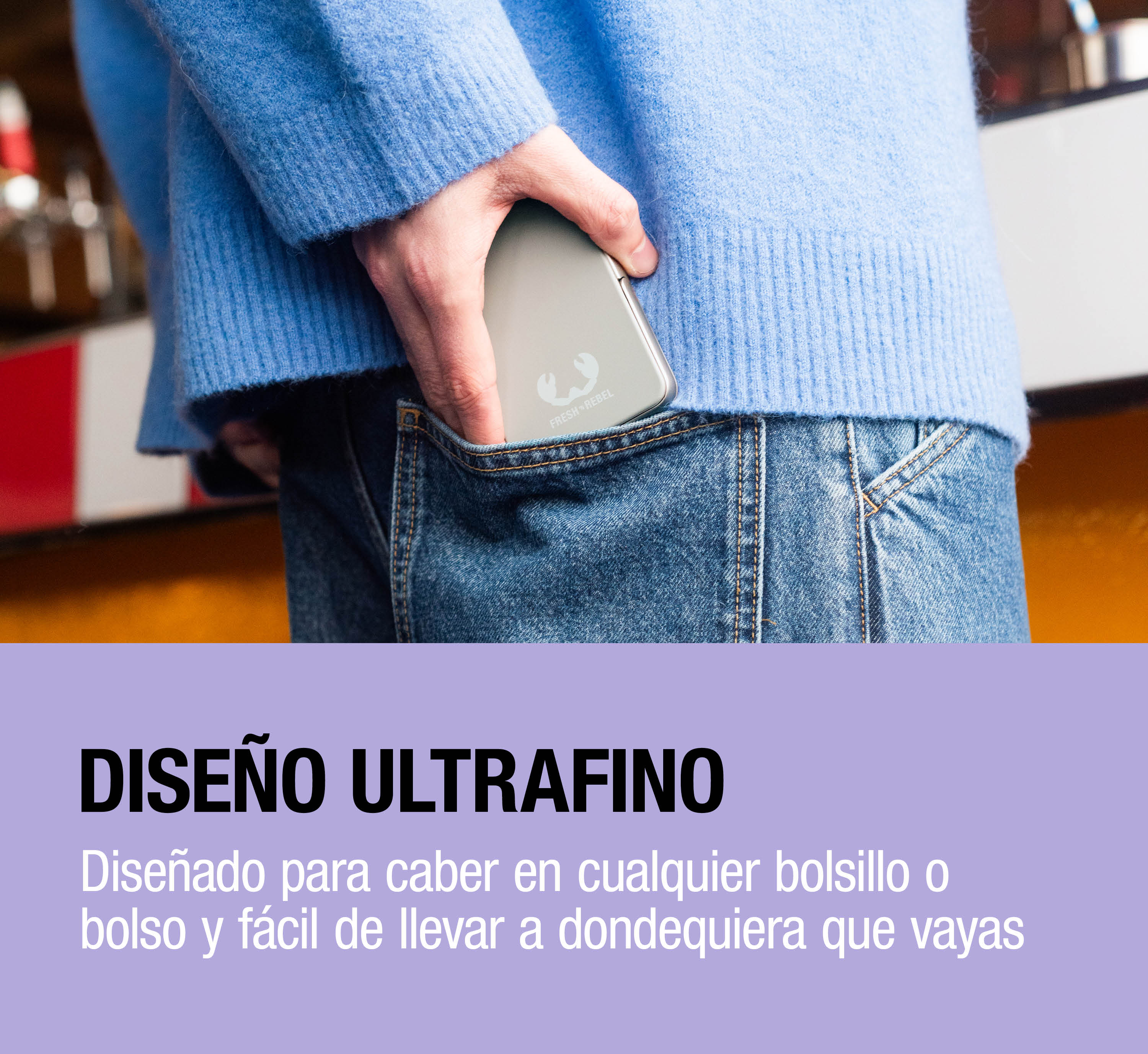 Una persona con maglione blu e jeans ripone una power bank argentata sottile nella tasca.