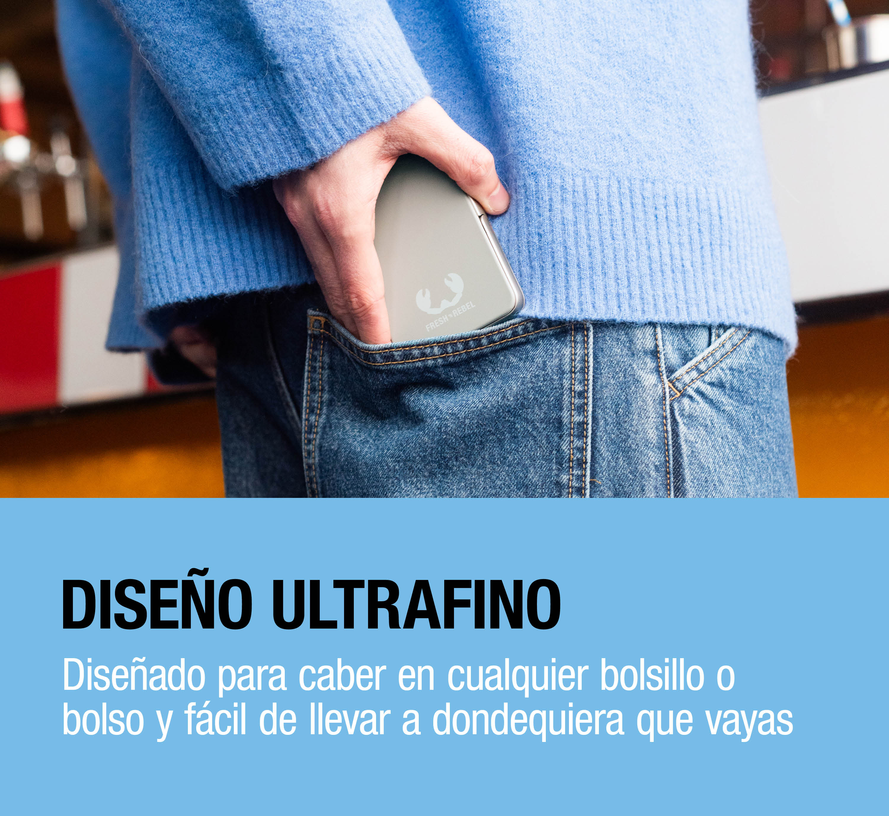 Una persona con maglione blu e jeans ripone una power bank argentata sottile nella tasca posteriore.