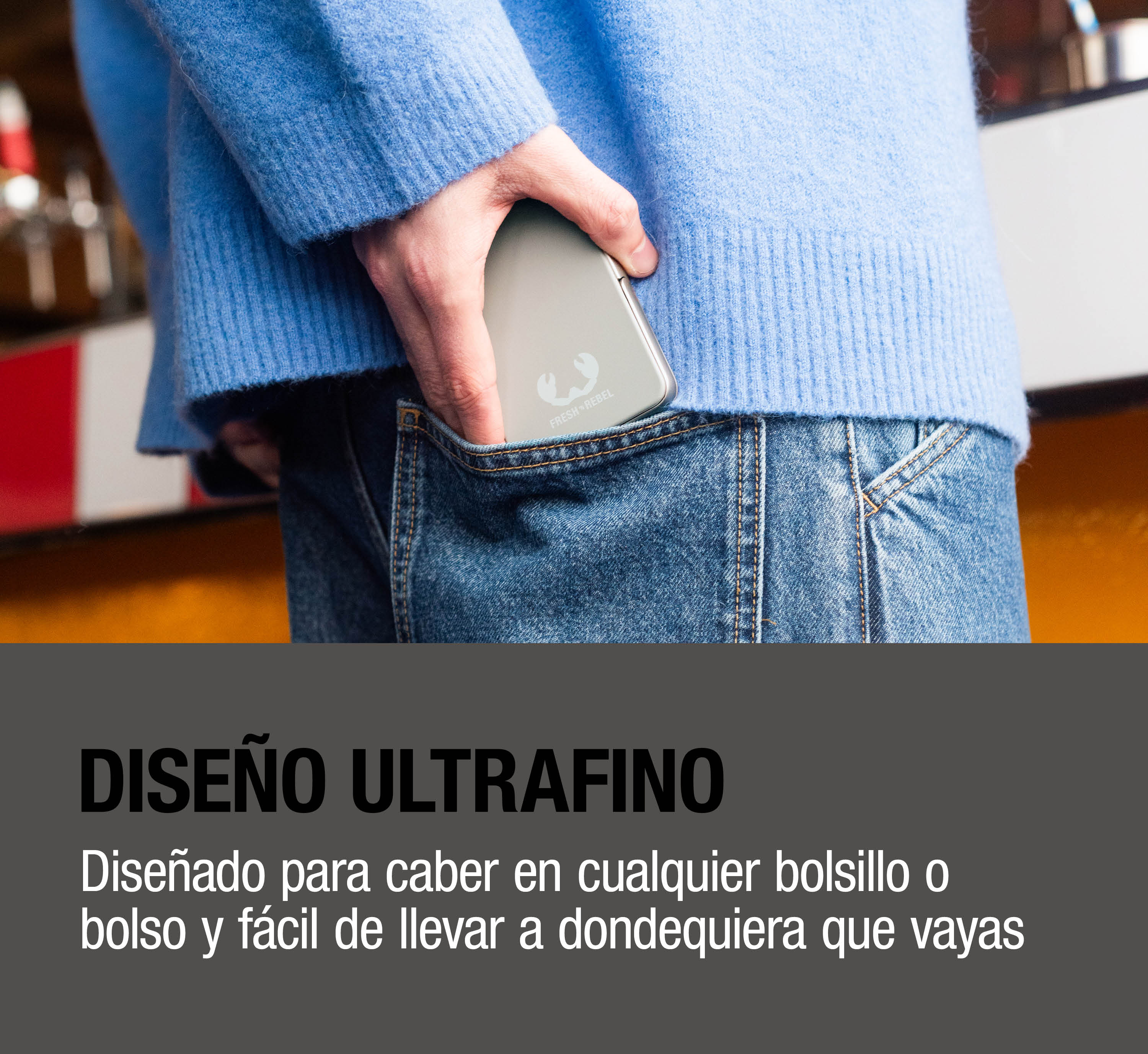 Persona con maglione blu ripone un dispositivo argentato Fresh 'n Rebel nella tasca dei jeans.