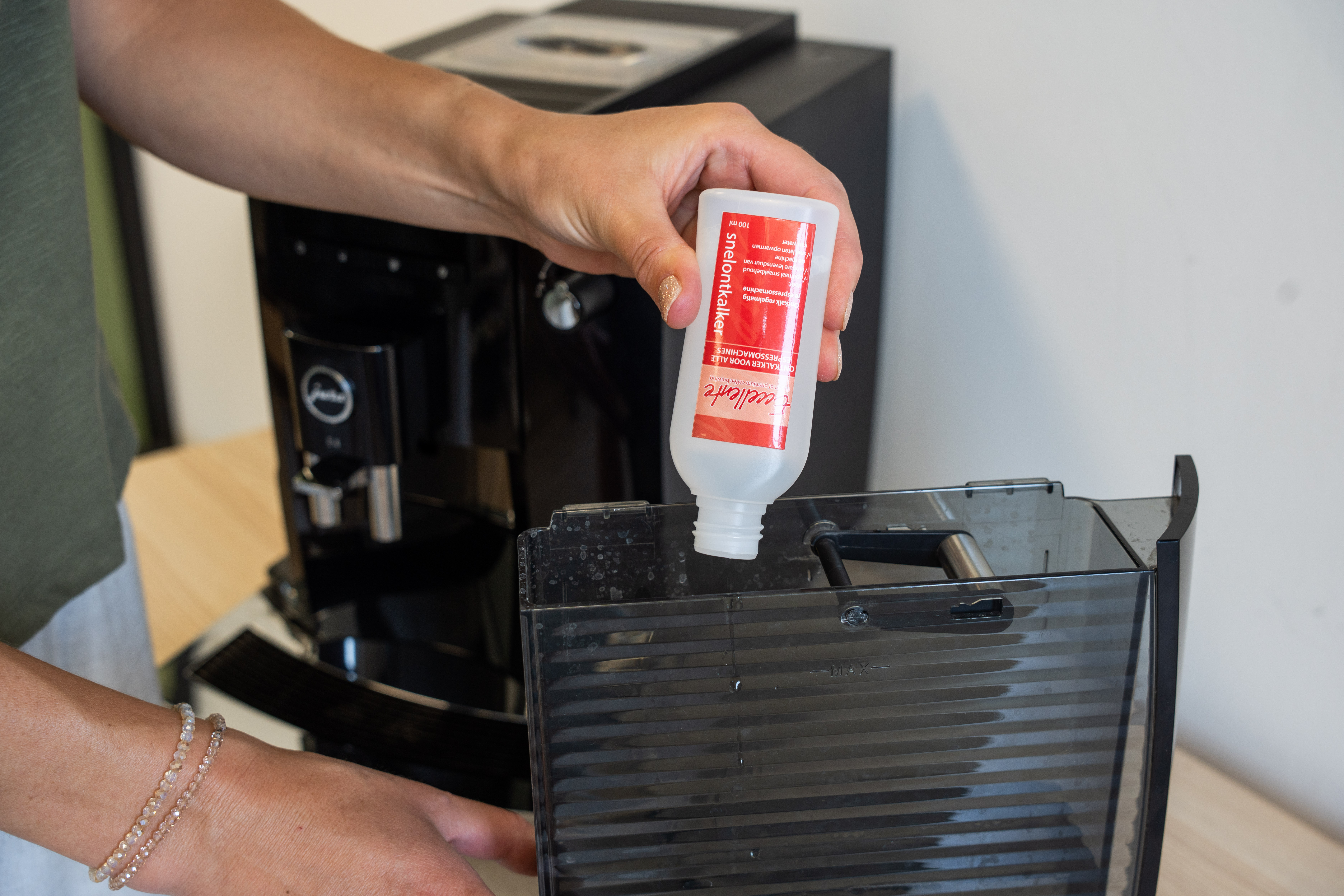 Une personne verse du détartrant d'une bouteille dans le réservoir d'eau d'une cafetière.