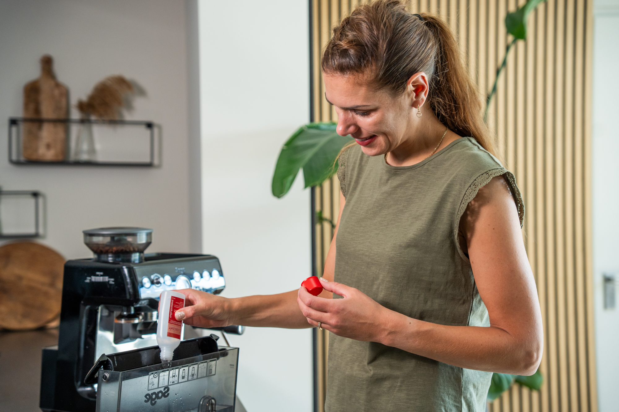 A woman pours descaling solution into a coffee machine water tank.