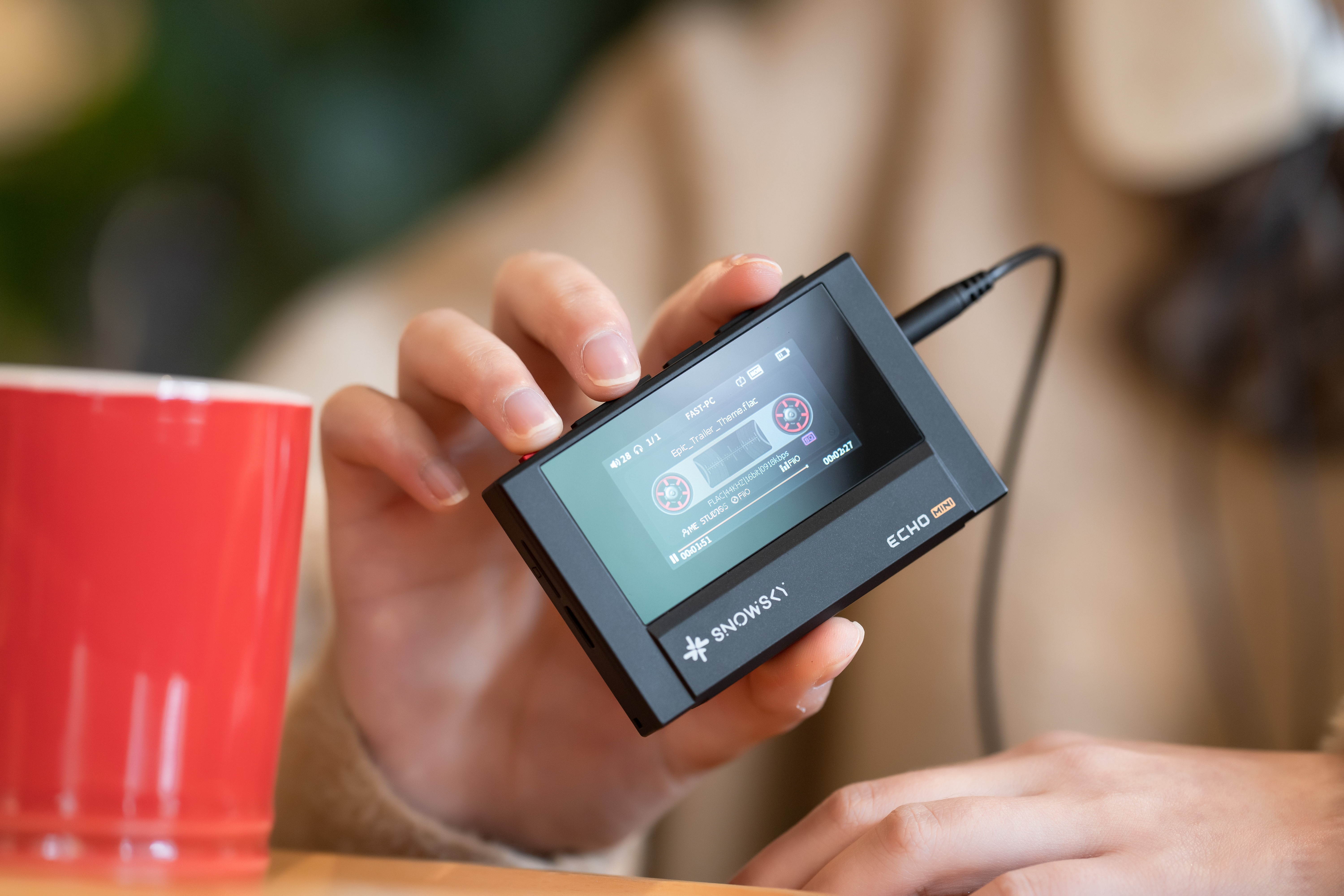 Alguien sostiene un reproductor negro Snowsky Echo Mini con pantalla, cerca de una taza roja.