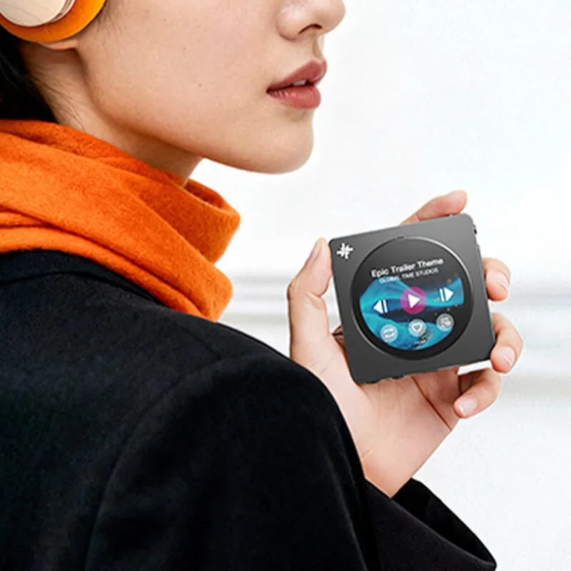 Una mujer con una bufanda naranja sostiene un pequeño reproductor de MP3 cuadrado con pantalla redonda.