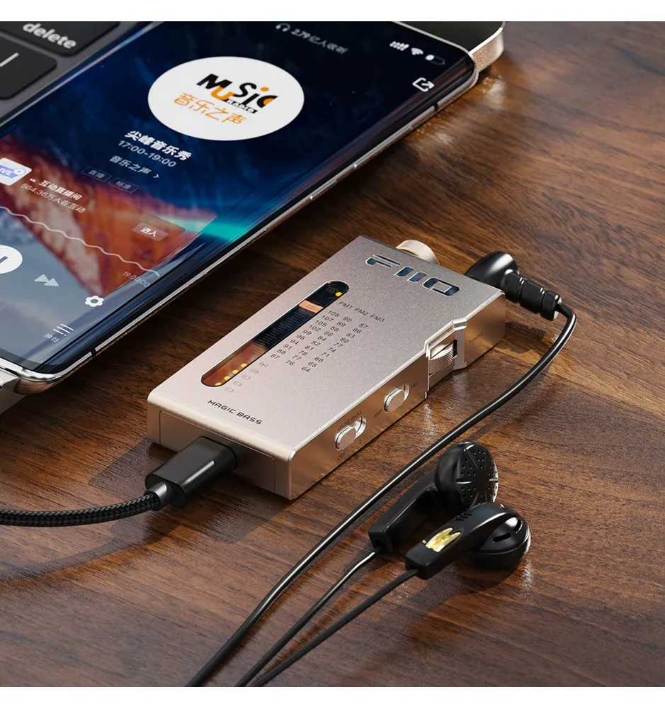 Un reproductor multimedia FiiO plateado con auriculares descansa sobre una mesa de madera junto a un teléfono.