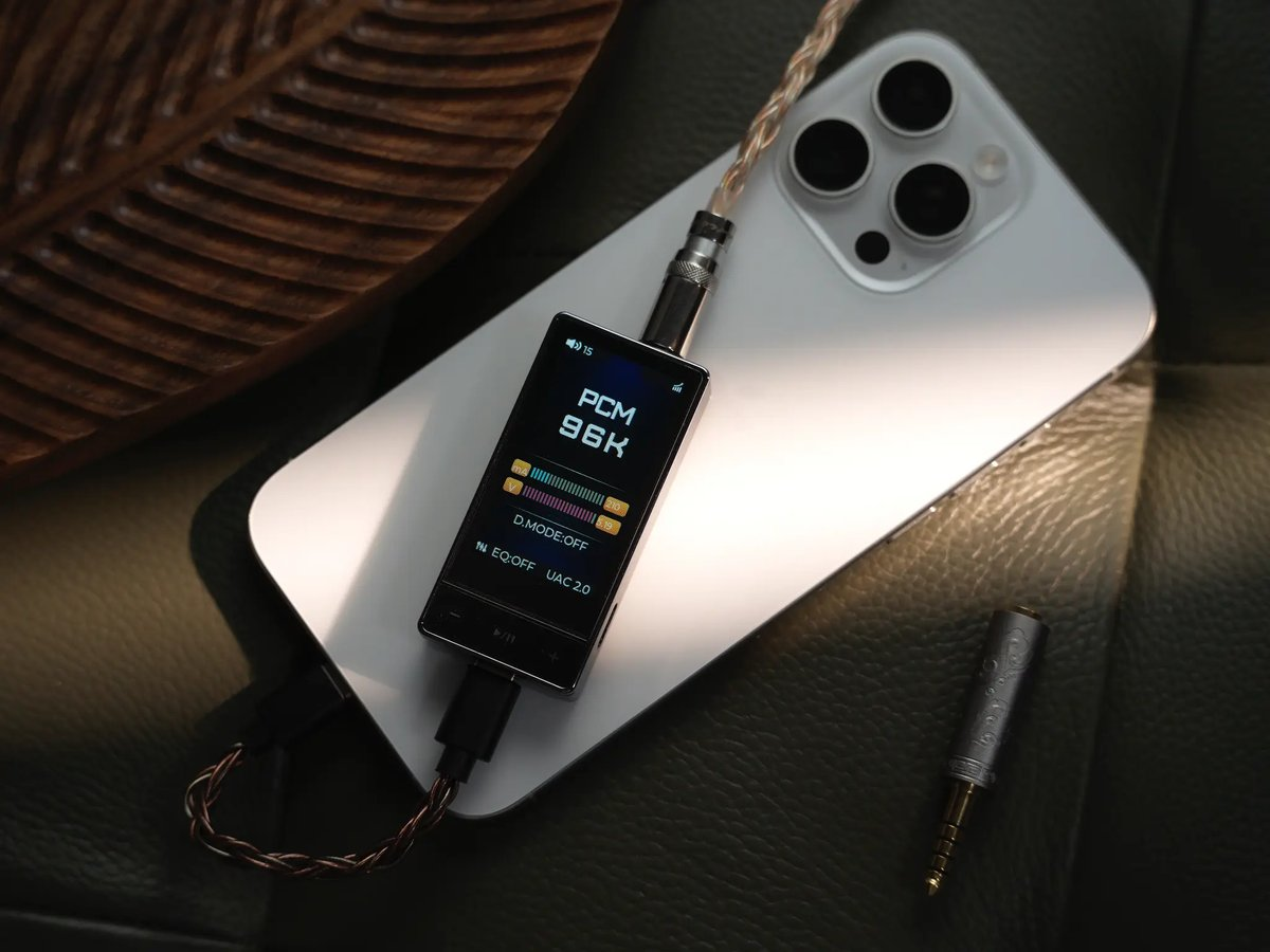 Un reproductor de audio portátil con pantalla descansa sobre un smartphone blanco, conectado con cables.