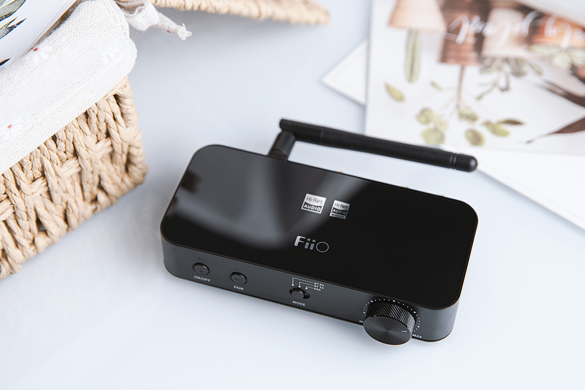 Un receptor de audio FiiO negro con antena, dial y botones en una superficie clara.